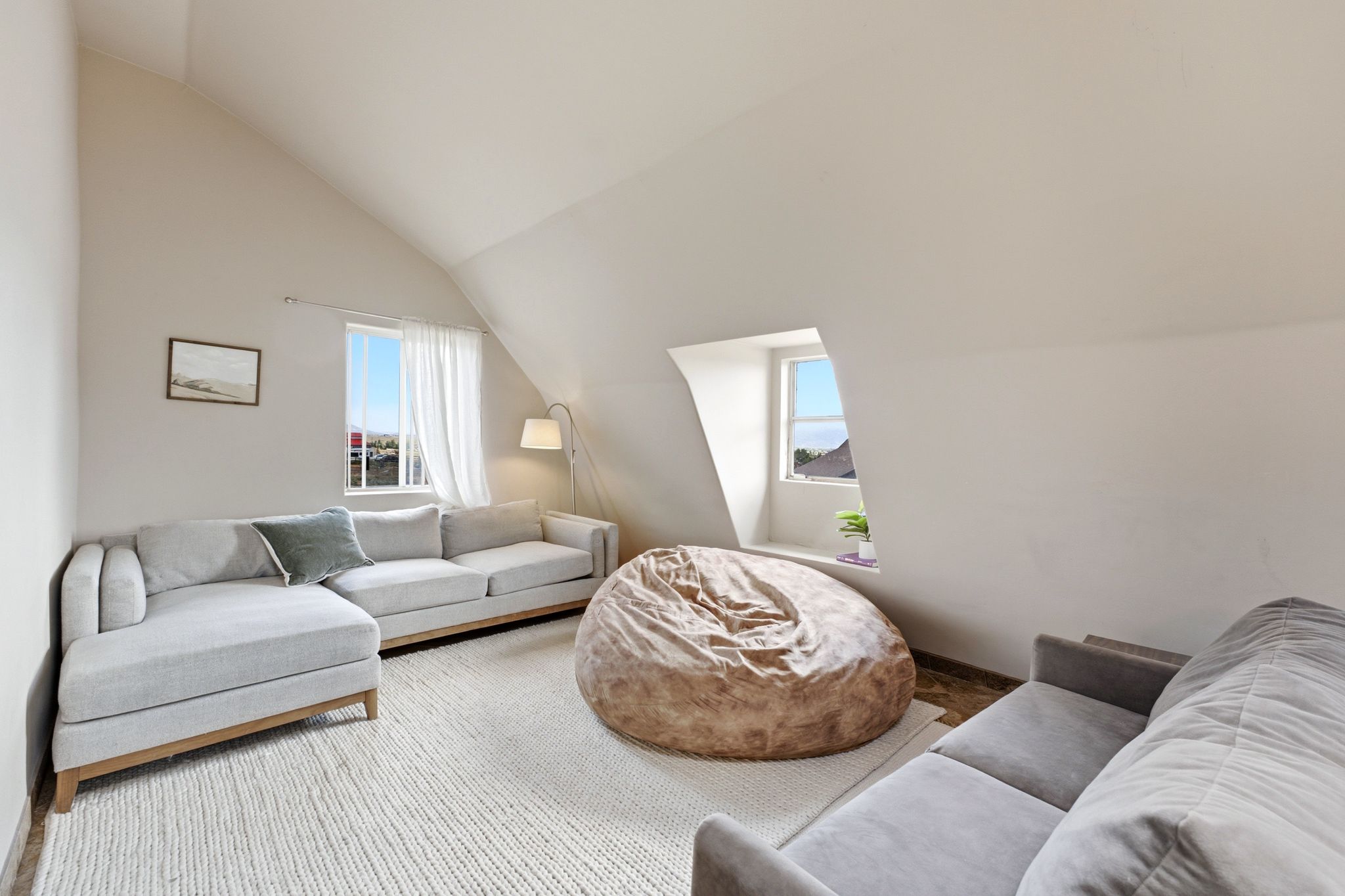 Attic living space featuring an angled ceiling, two windows, and a light-toned area rug over wood-finish flooring