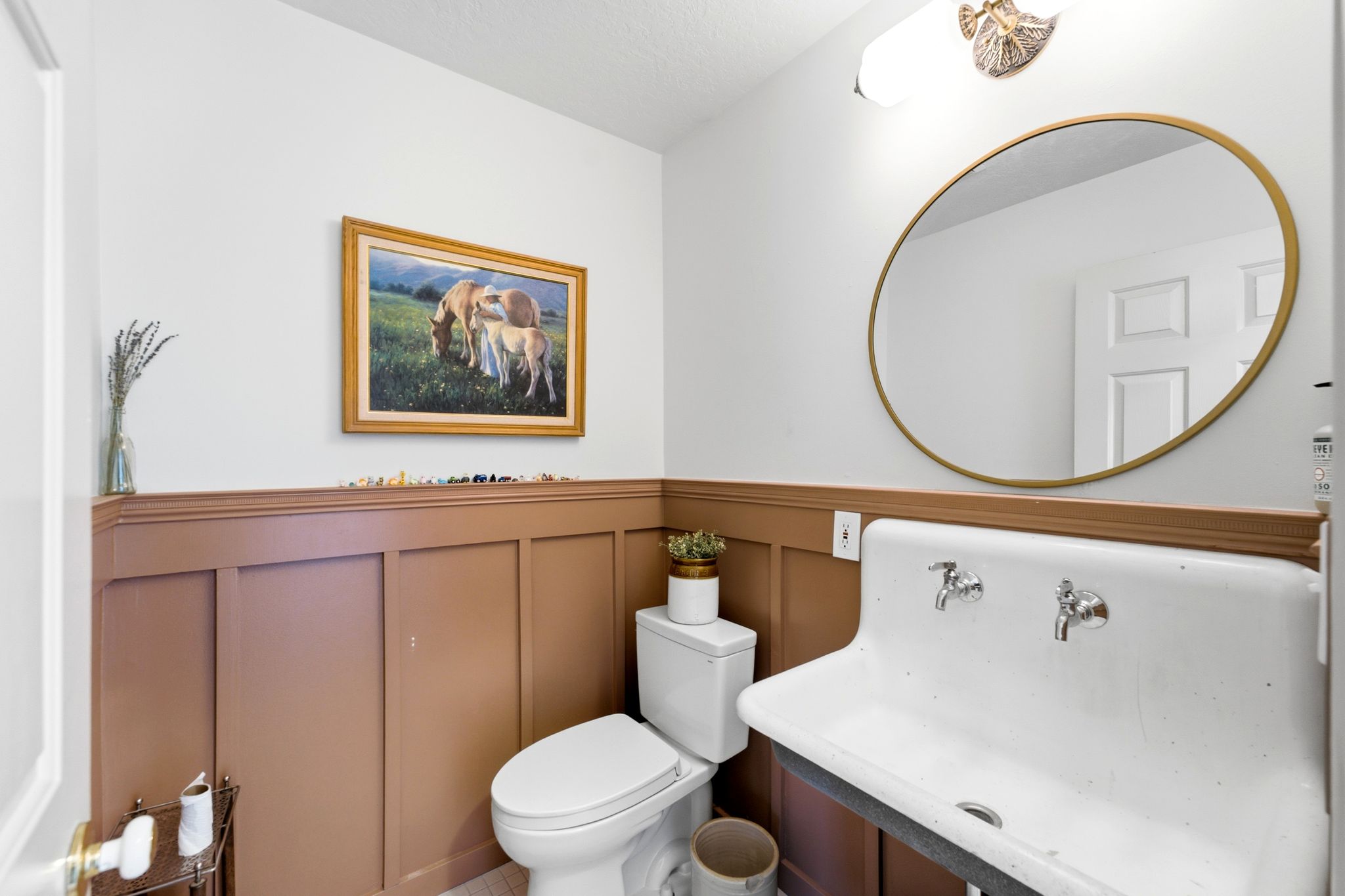 Half bath featuring wainscoting, a wall-mounted sink with dual faucets, and a contemporary round mirror