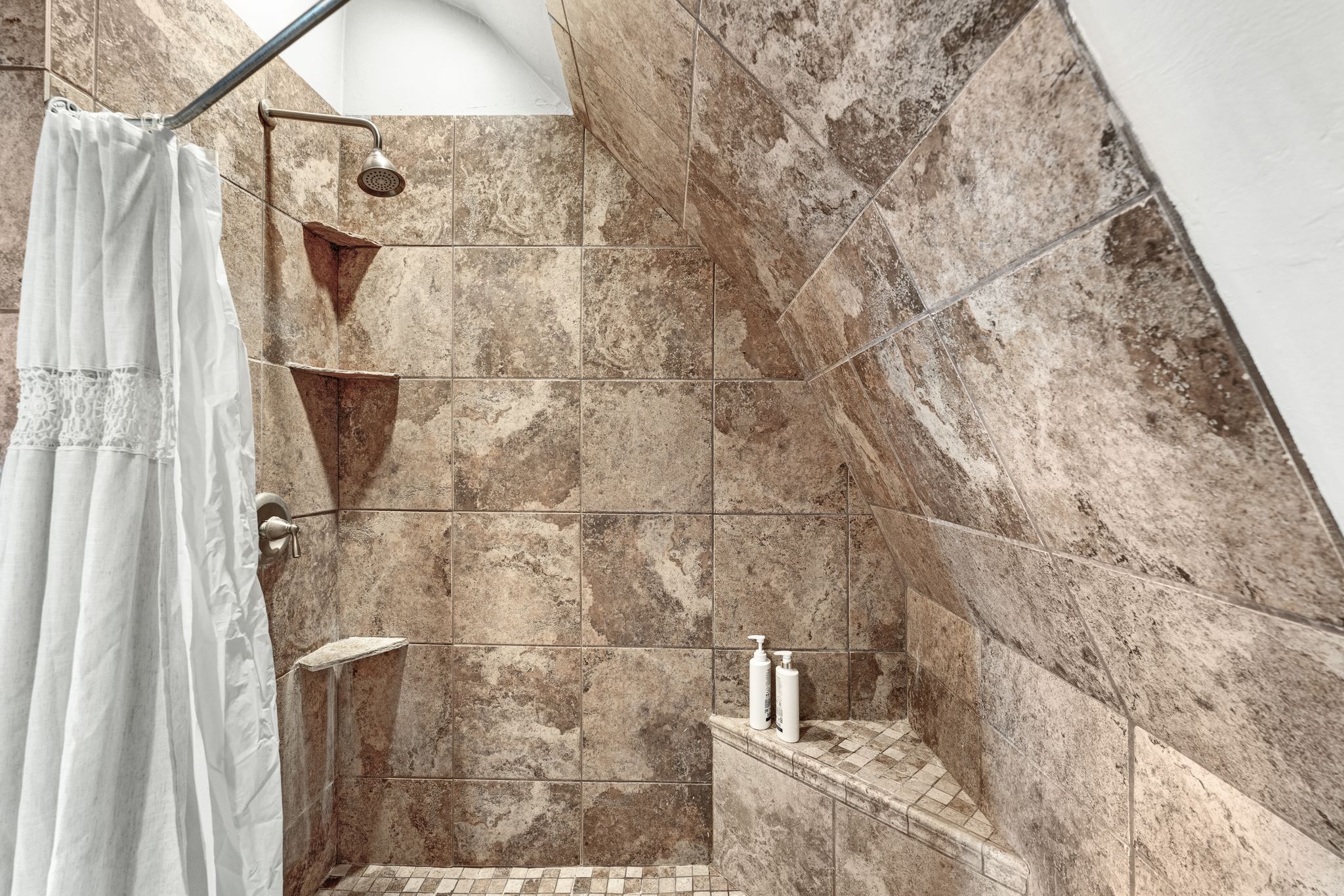 Tiled shower featuring a sloped ceiling, built-in shelving, and a mosaic tile floor