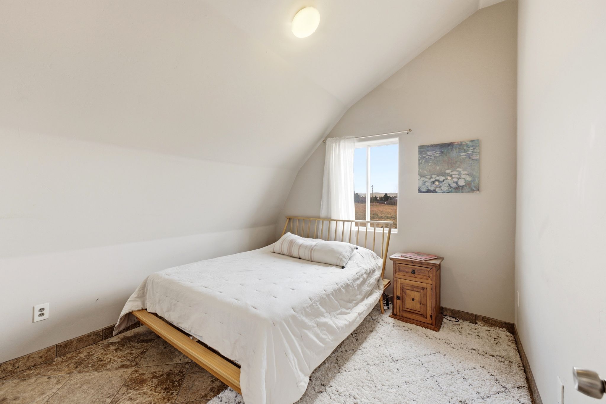 Vaulted ceiling bedroom featuring a single window with white sheer curtains, a flush-mount ceiling light, and neutral wall tones