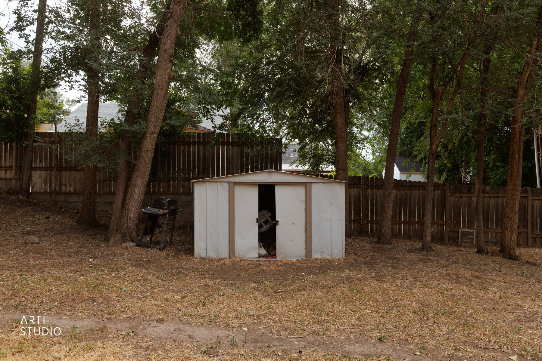 Rear yard featuring a storage shed with an open doorway, mature trees, and a wood privacy fence