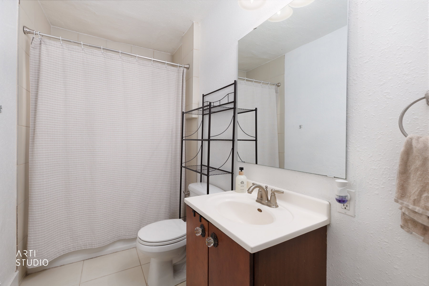Bathroom featuring a shower with tiled surround, a toilet, a vanity with a white countertop and integrated sink, a wall-mounted mirror, and a towel ring
