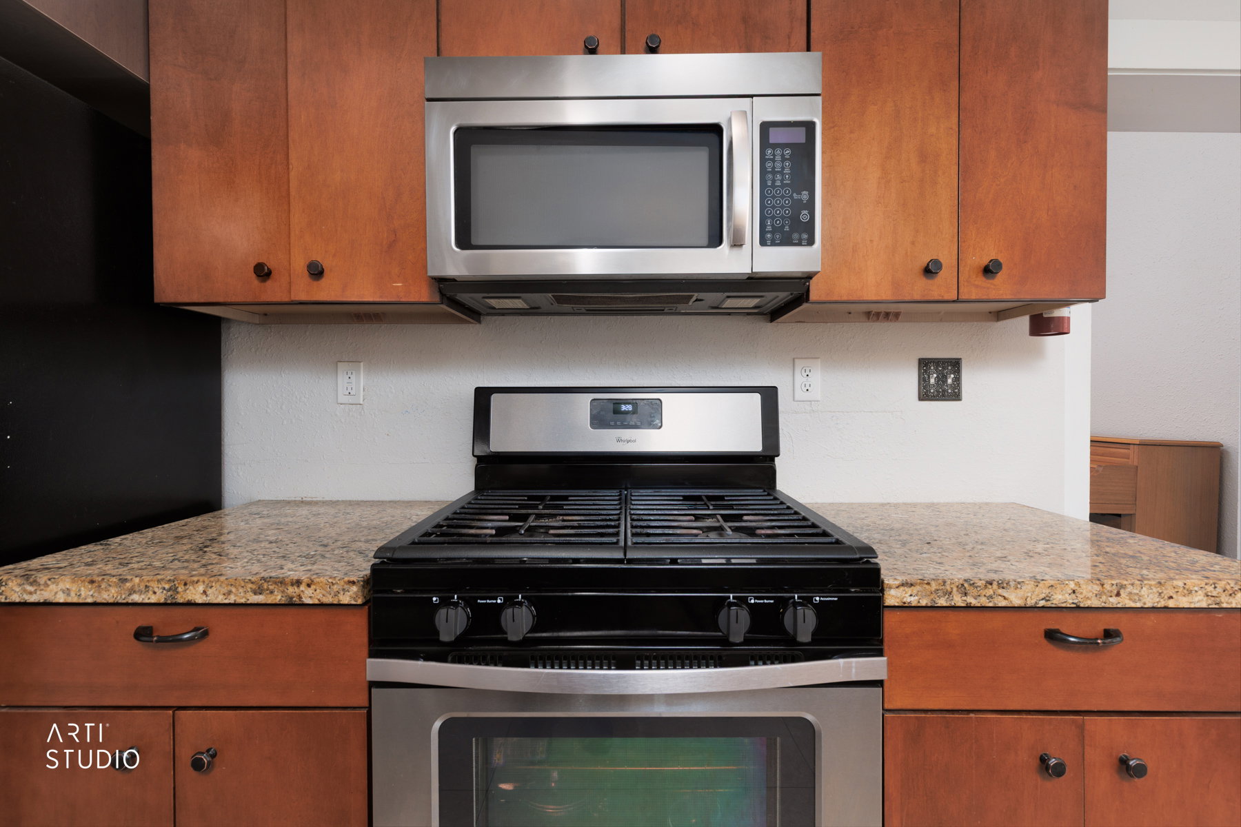 Kitchen featuring a stainless steel range with overhead microwave, wood cabinetry, and speckled countertops