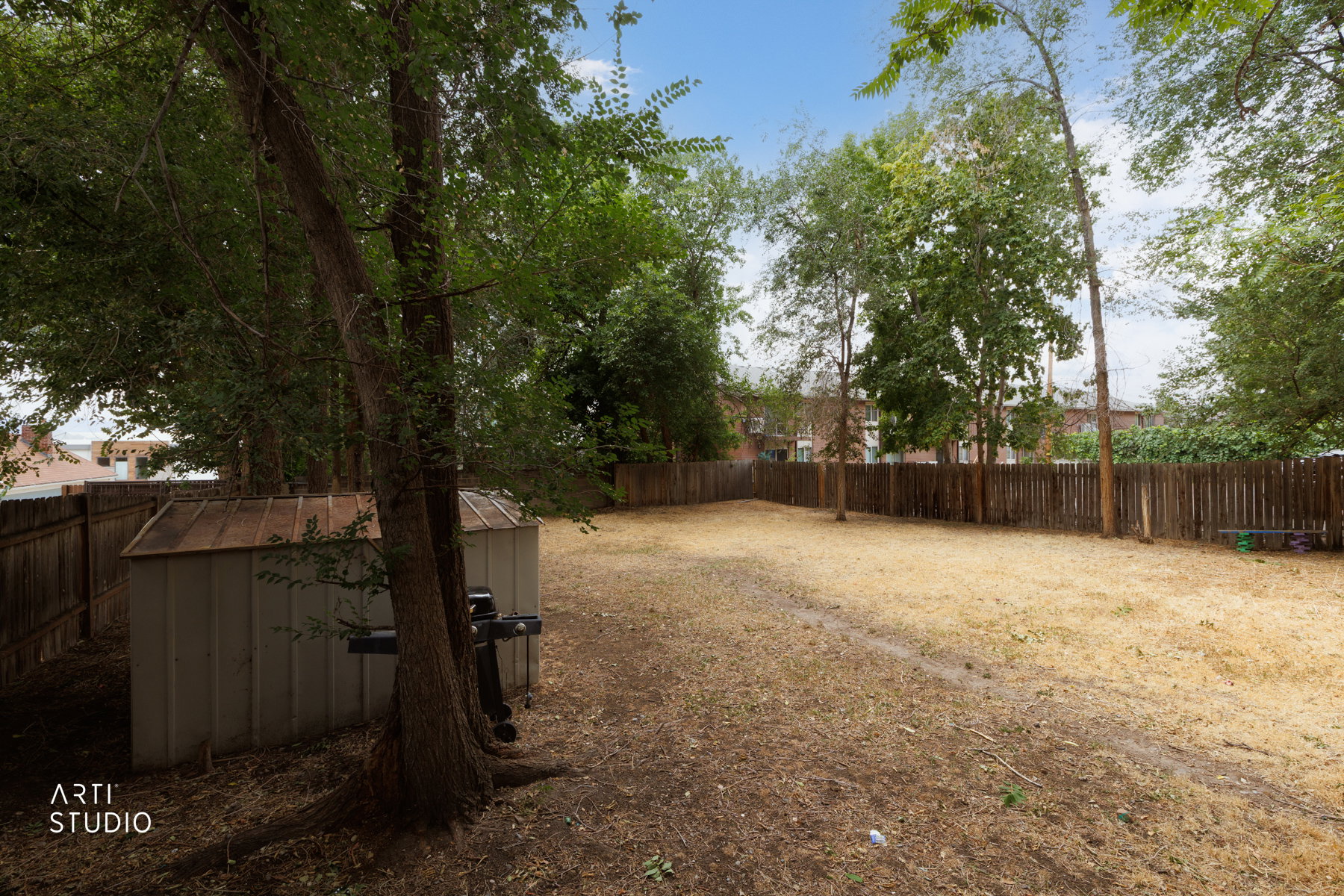Expansive backyard featuring a wood privacy fence, mature trees, and a metal storage shed