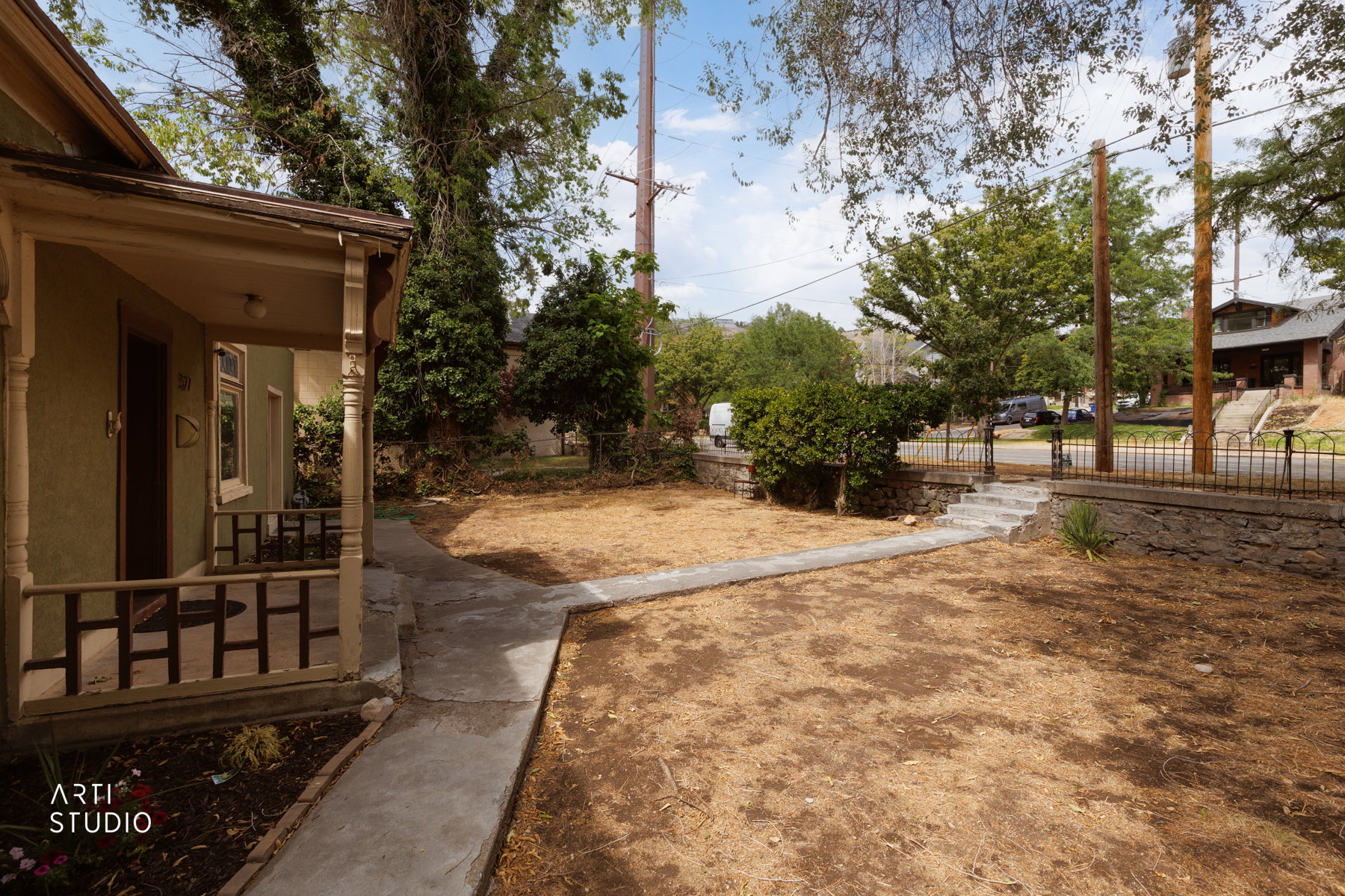 Front yard featuring a concrete walkway, established perimeter fencing, and mature trees