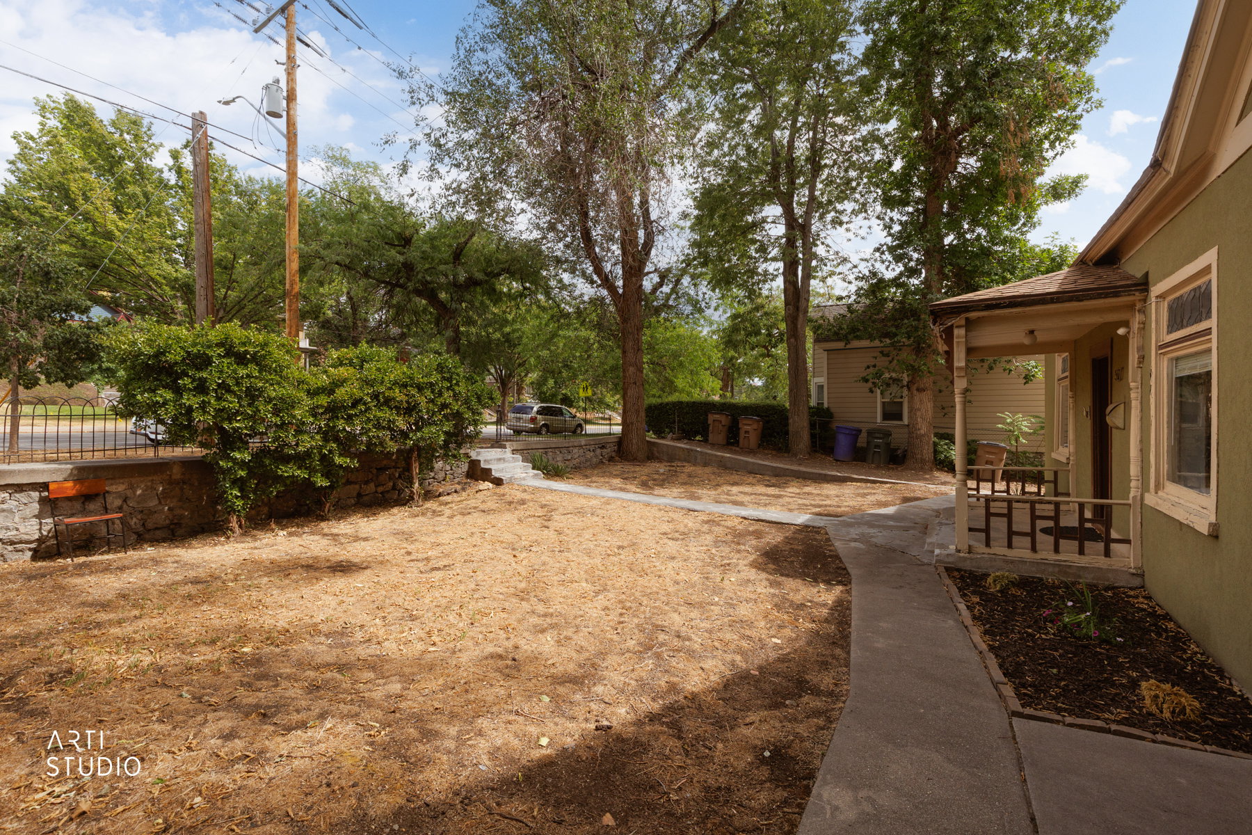 Front exterior featuring a covered porch with a railing, a concrete pathway, and mature trees