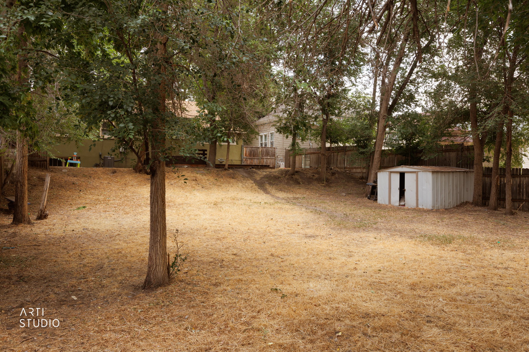 Expansive backyard featuring mature trees, a wood privacy fence, and a metal storage shed