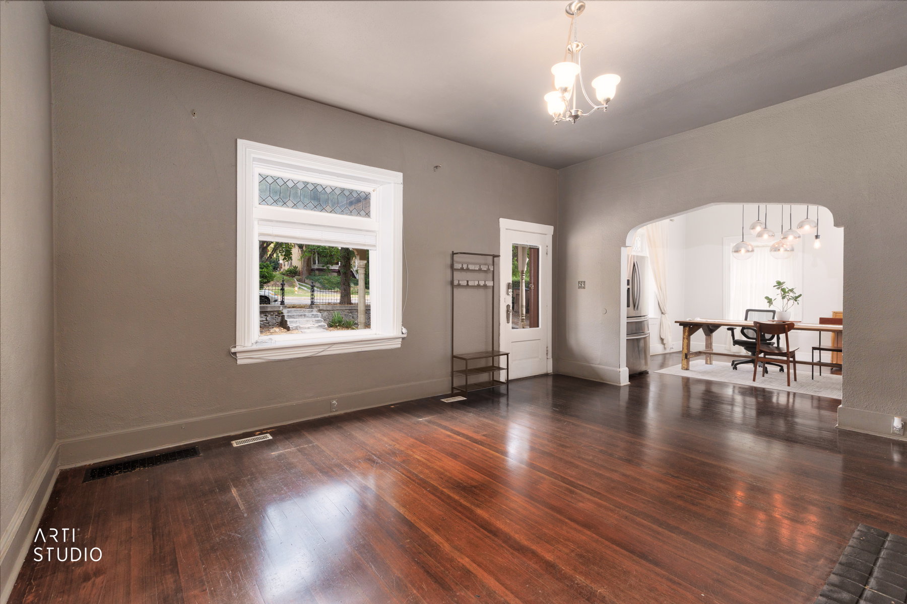 Spacious room featuring polished wood flooring, a window with leaded glass transom, and an arched entryway