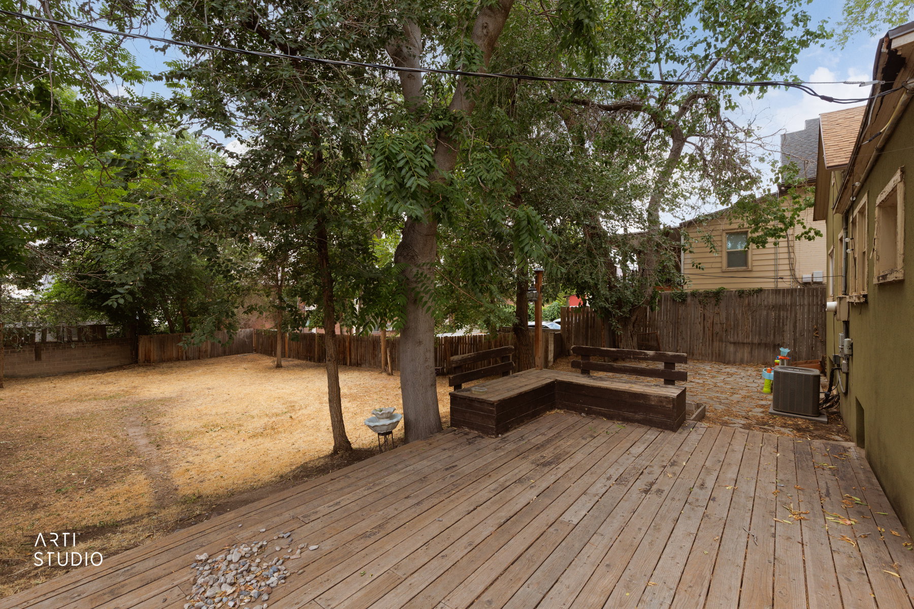 Spacious backyard featuring a large wood deck, built-in deck seating, mature trees, and a wooden privacy fence