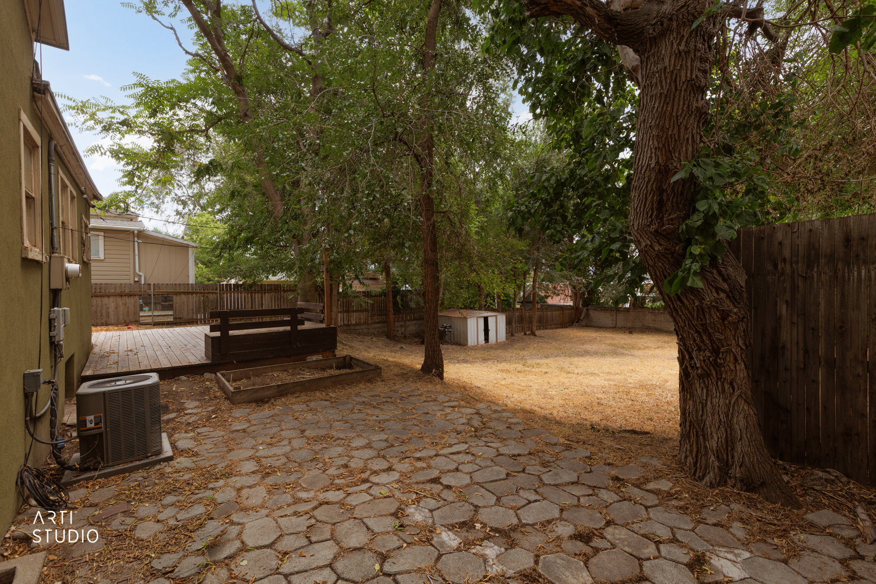 Spacious backyard featuring a multi-level wooden deck, stone paver patio, mature trees, and a wooden privacy fence