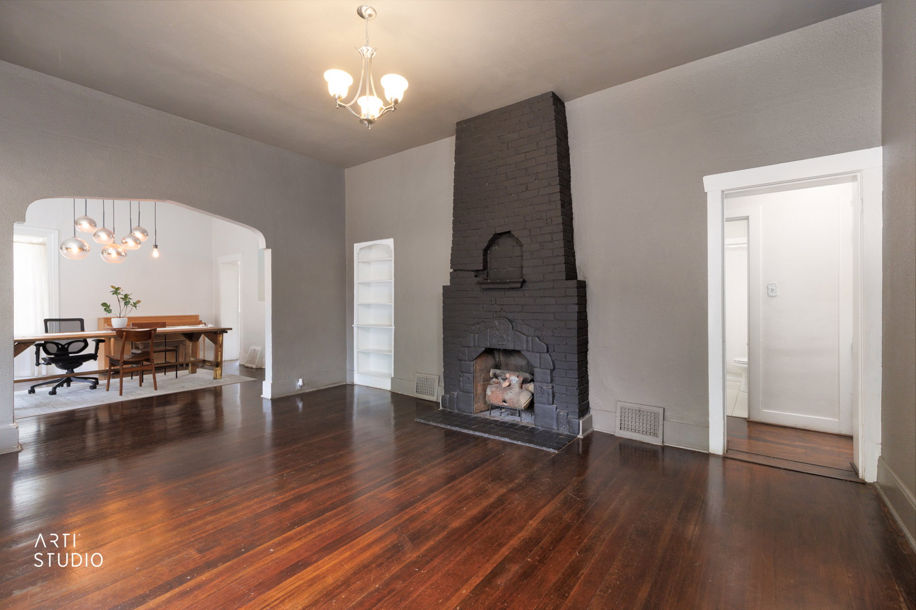 Spacious room featuring rich wood-finish flooring, a dark brick fireplace, and an arched entry to an additional space