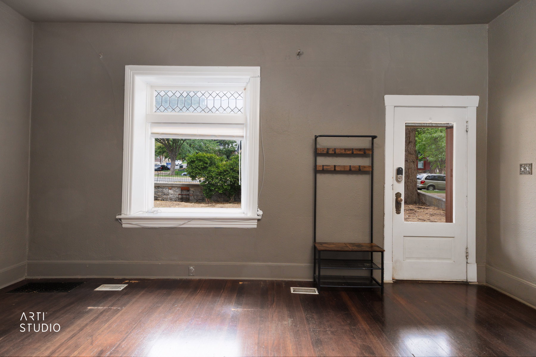 Hardwood flooring throughout featuring a window with leaded glass transom and a white paneled door with a glass insert