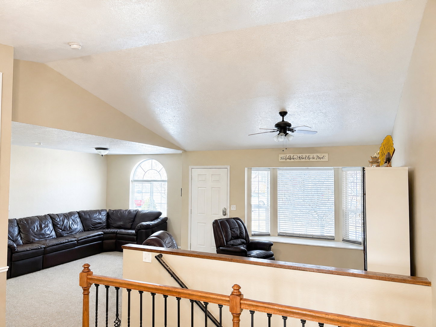 Vaulted ceilings highlight the living area, featuring a decorative ceiling fan, bay window with blinds, and an arched window