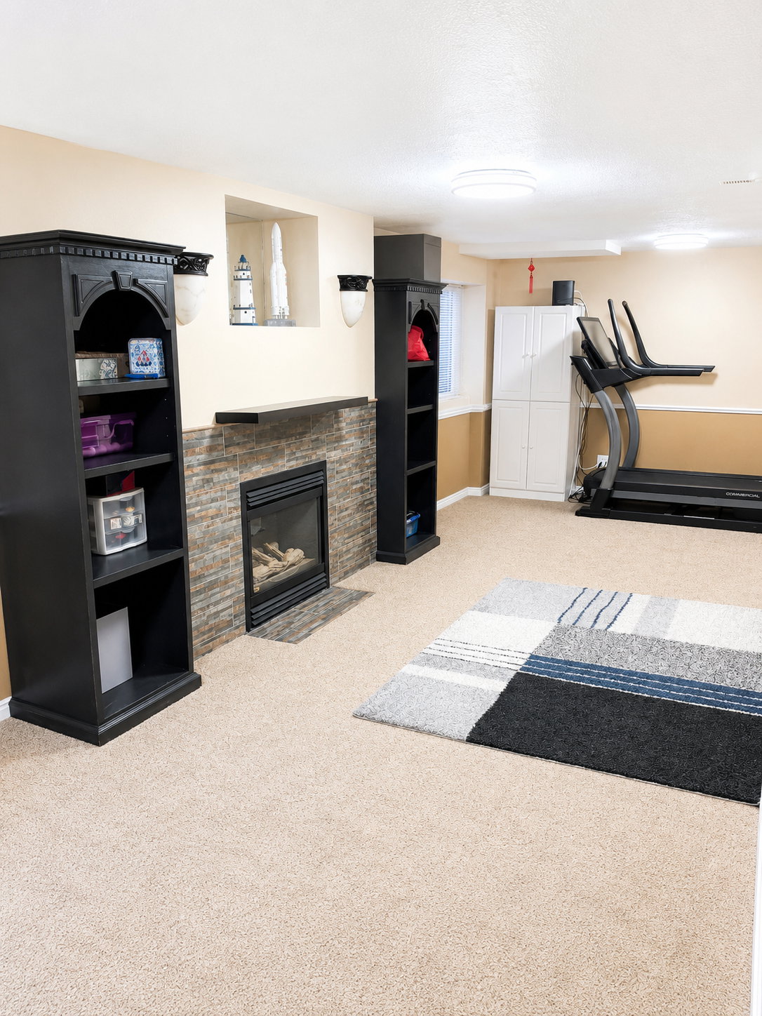 Recreational space featuring wall-to-wall carpeting, stone-faced fireplace with hearth, built-in shelving, recessed display nook, and overhead lighting