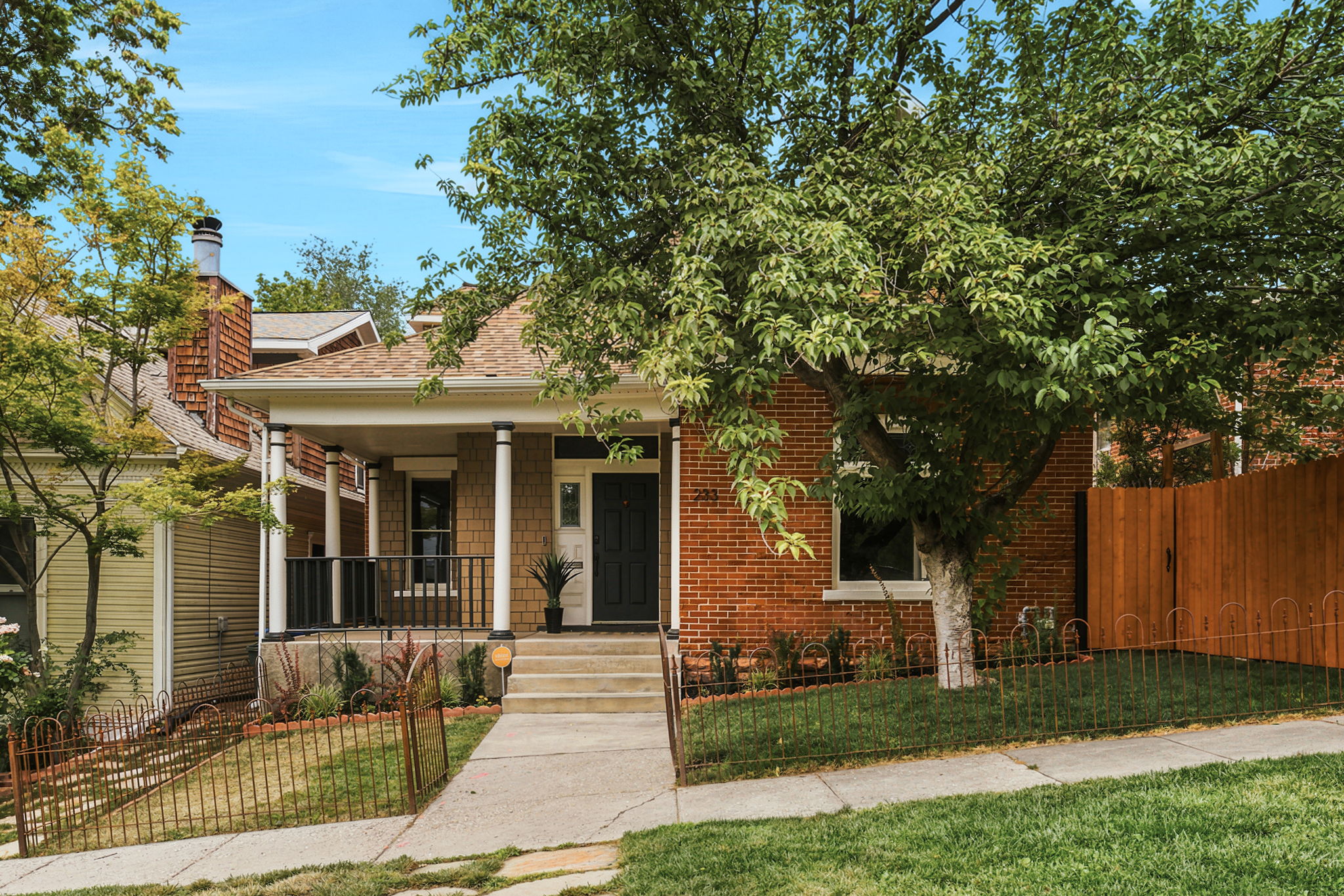 Classic brick exterior featuring a covered front porch, white columns, black railings, and a dark entry door