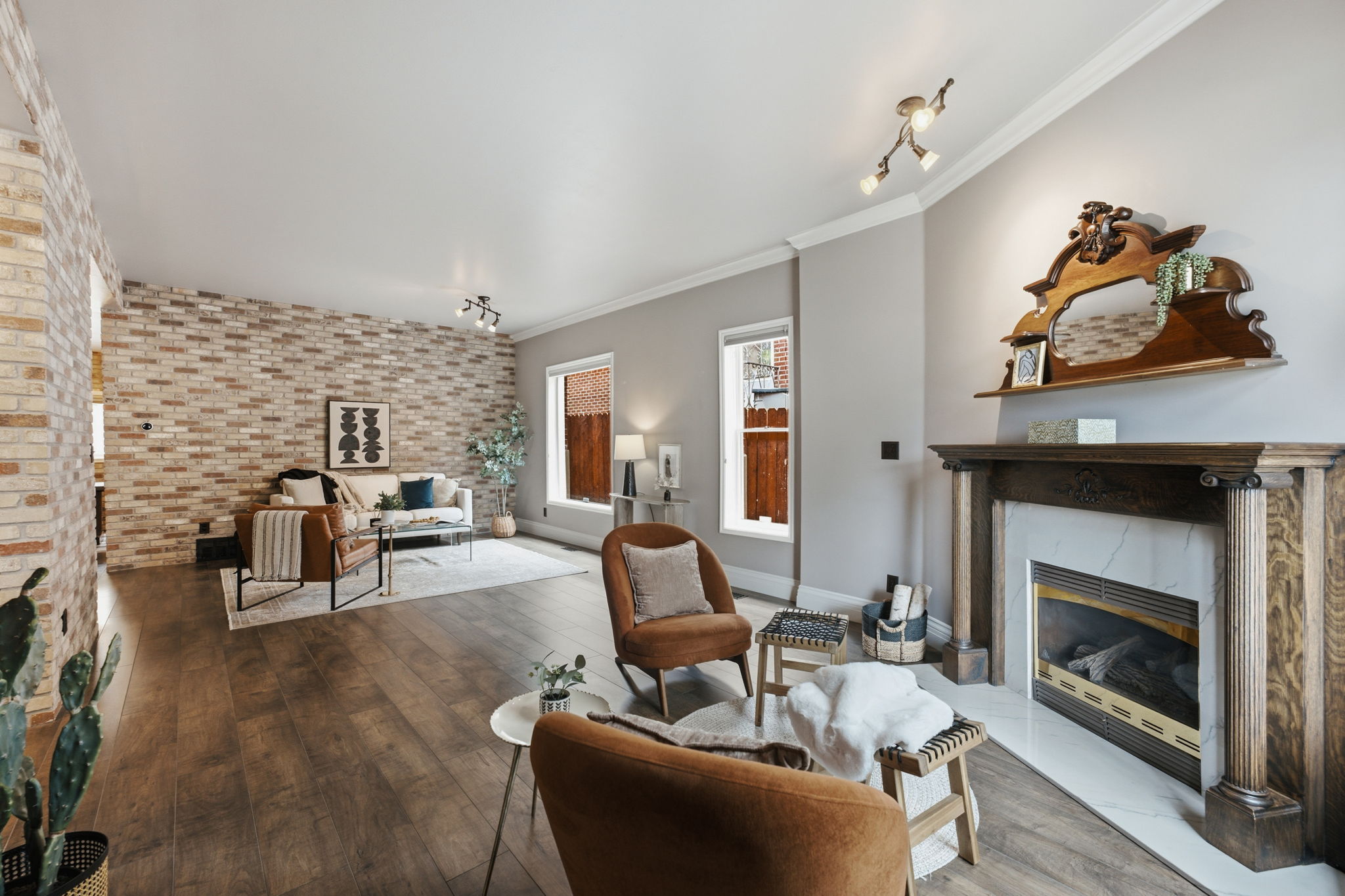 Spacious living area featuring wood-finish flooring, a brick accent wall, and a fireplace with a wood mantle and marble surround