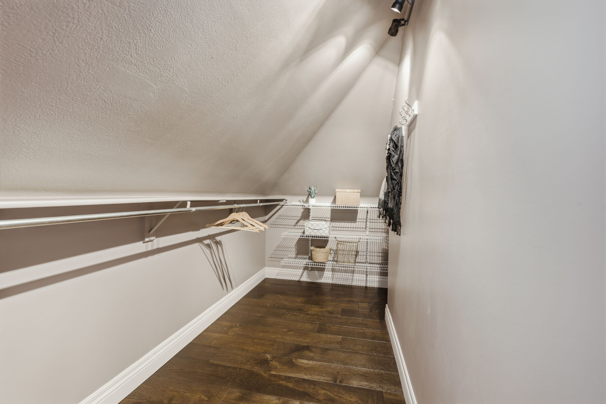 Attic storage area featuring wood-finish flooring, track lighting, and built-in wire shelving