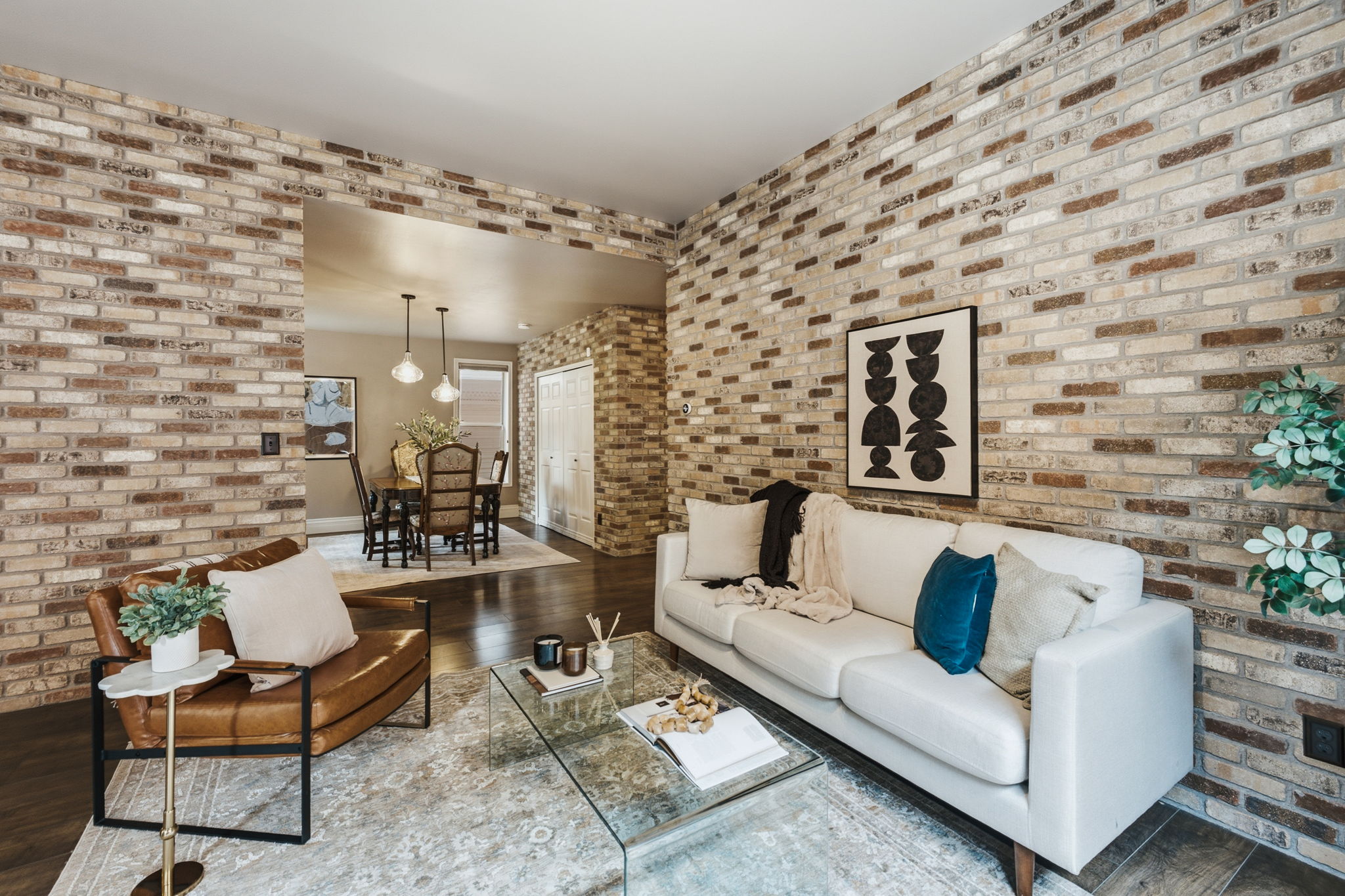 Interior living space featuring exposed brick walls, dark wood-finish flooring, and an open architectural feature to a dining area