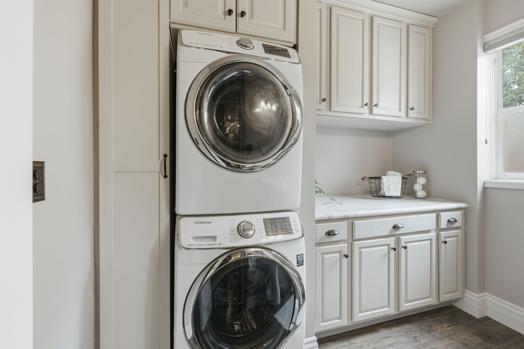 Dedicated laundry space featuring a stacked washer and dryer, white shaker-style cabinetry, a built-in countertop, and a window for natural light