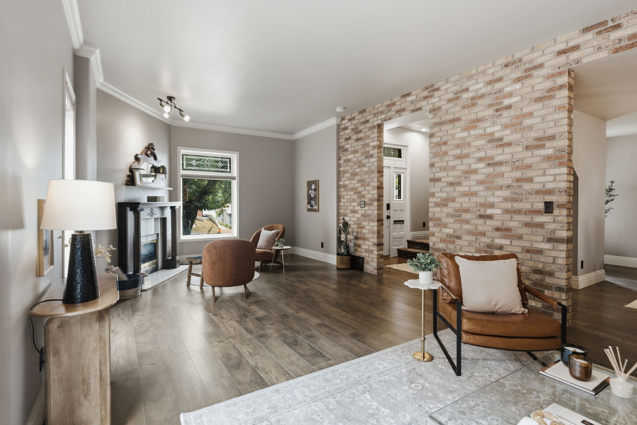 Open-concept living space featuring wood-finish flooring, a brick accent wall, a fireplace with a black mantel, and crown molding