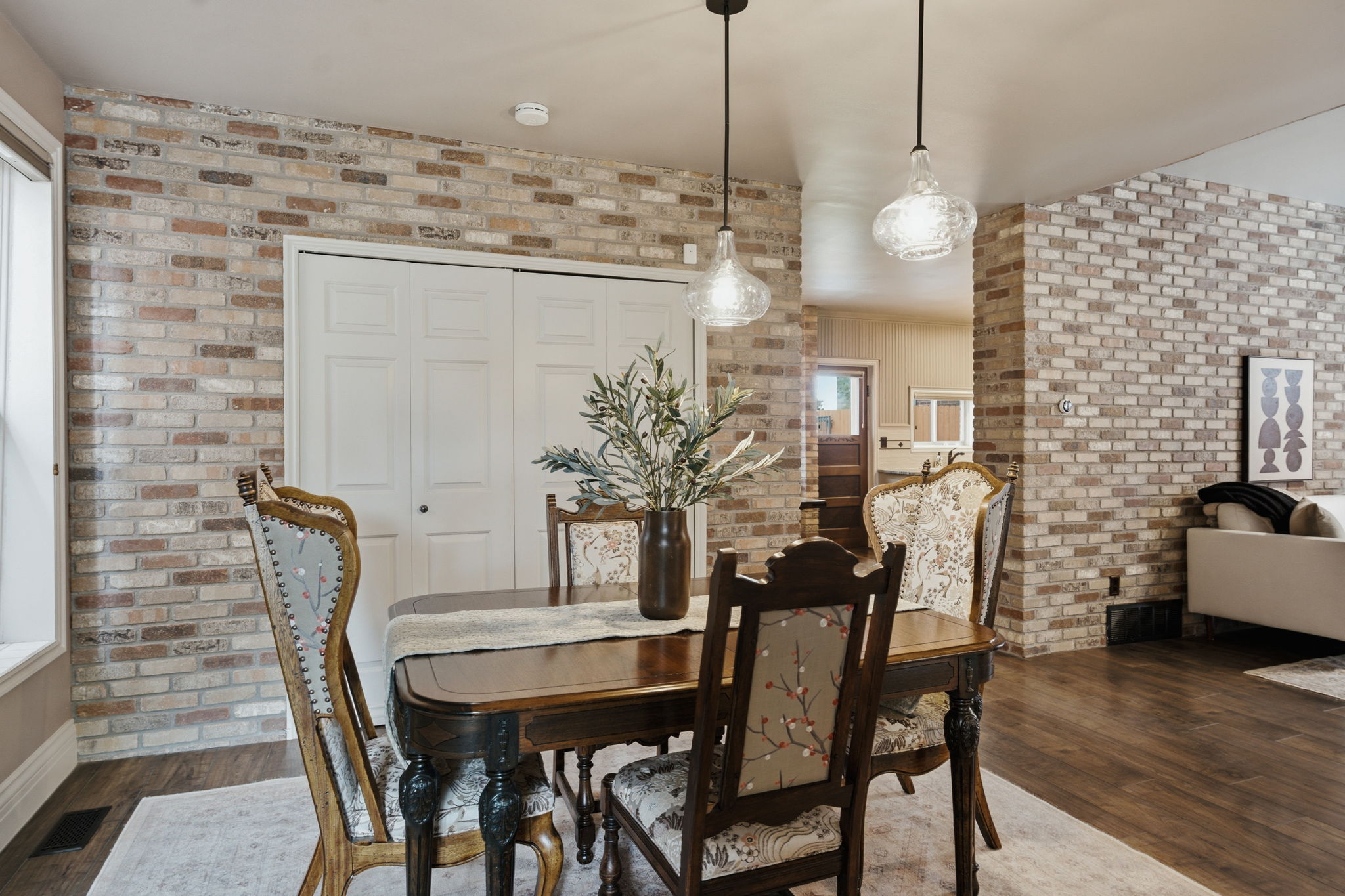 Dining area featuring multi-toned brick accent walls, wood-finish flooring, and white bi-fold closet doors