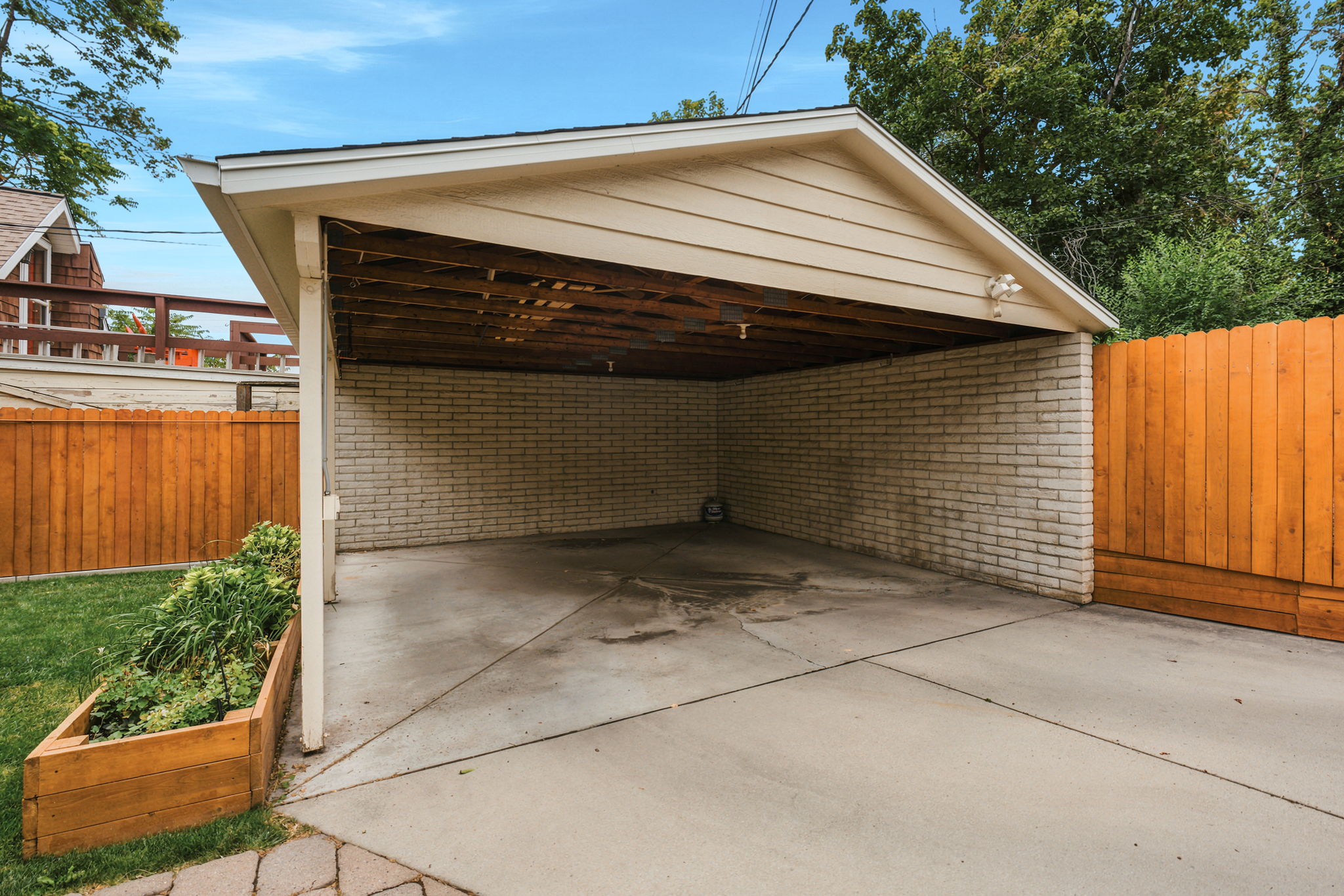 Covered carport featuring a concrete pad, light brick wall, and horizontal siding