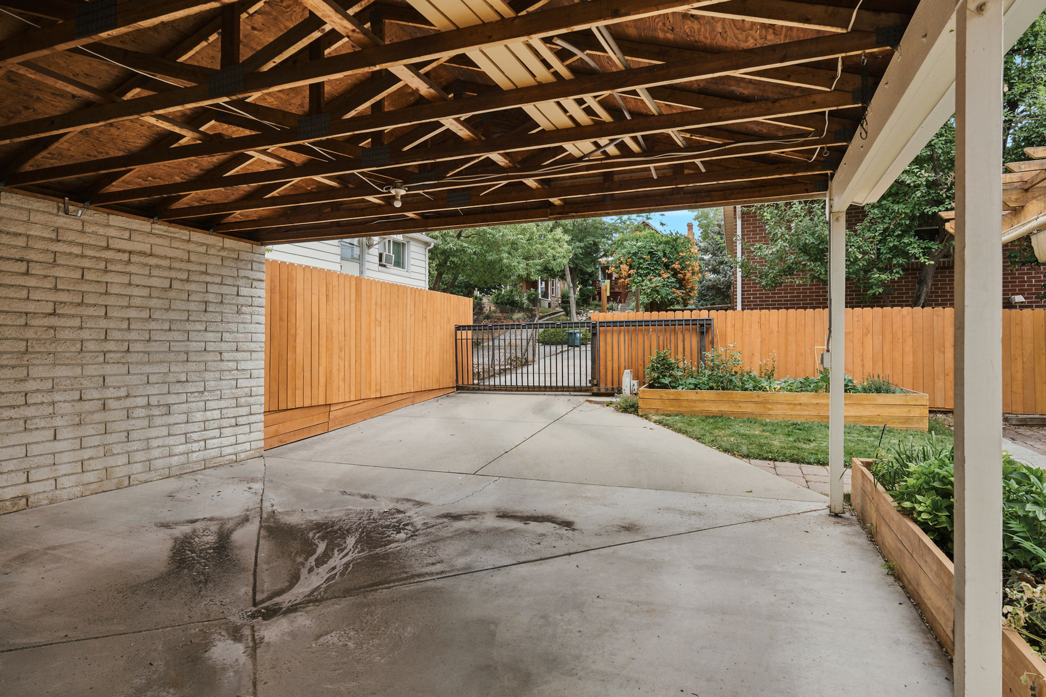 Covered concrete patio featuring an exposed wood beam ceiling, white brick wall, and privacy fencing