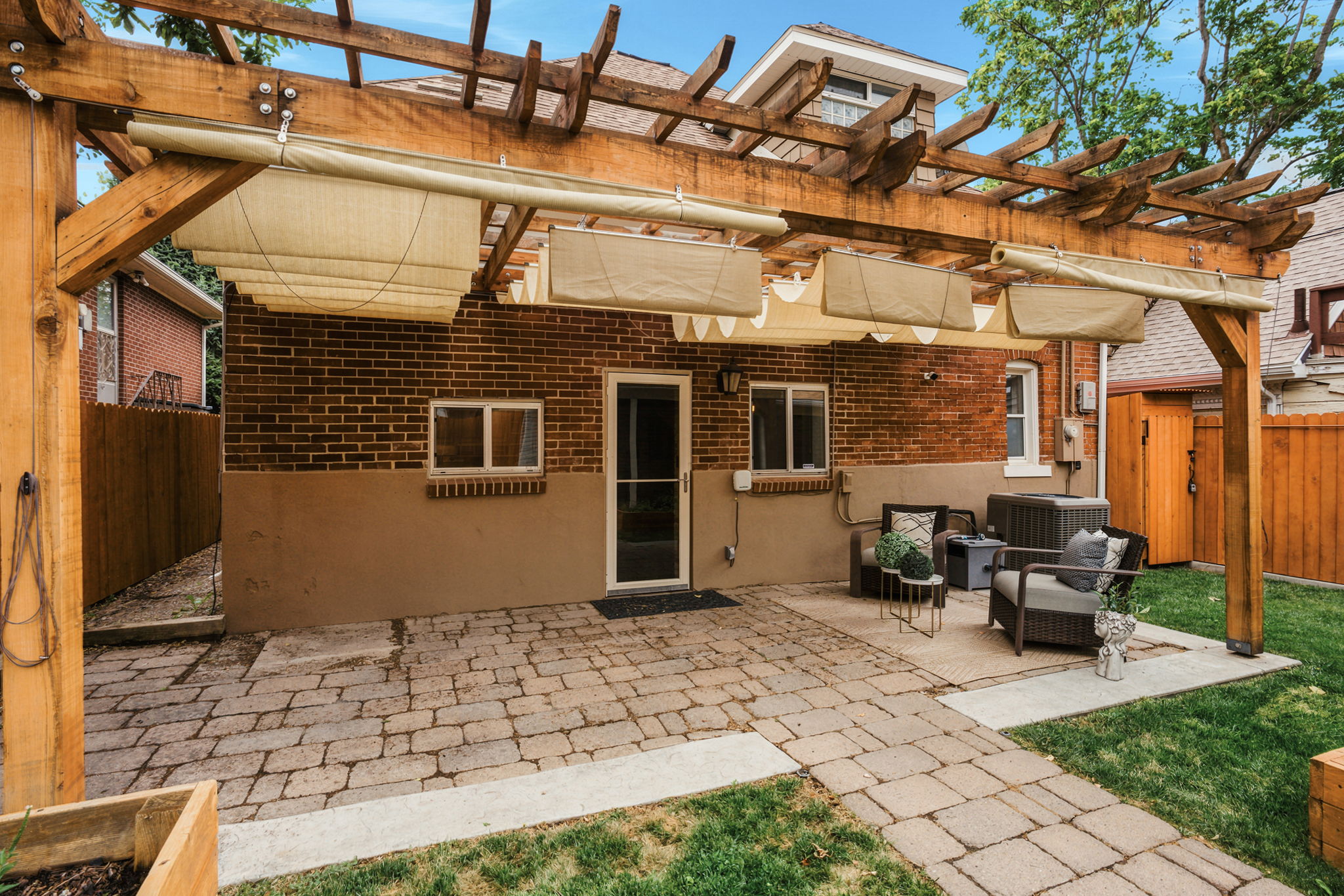 Expansive paver patio with a timber pergola featuring retractable canvas shades