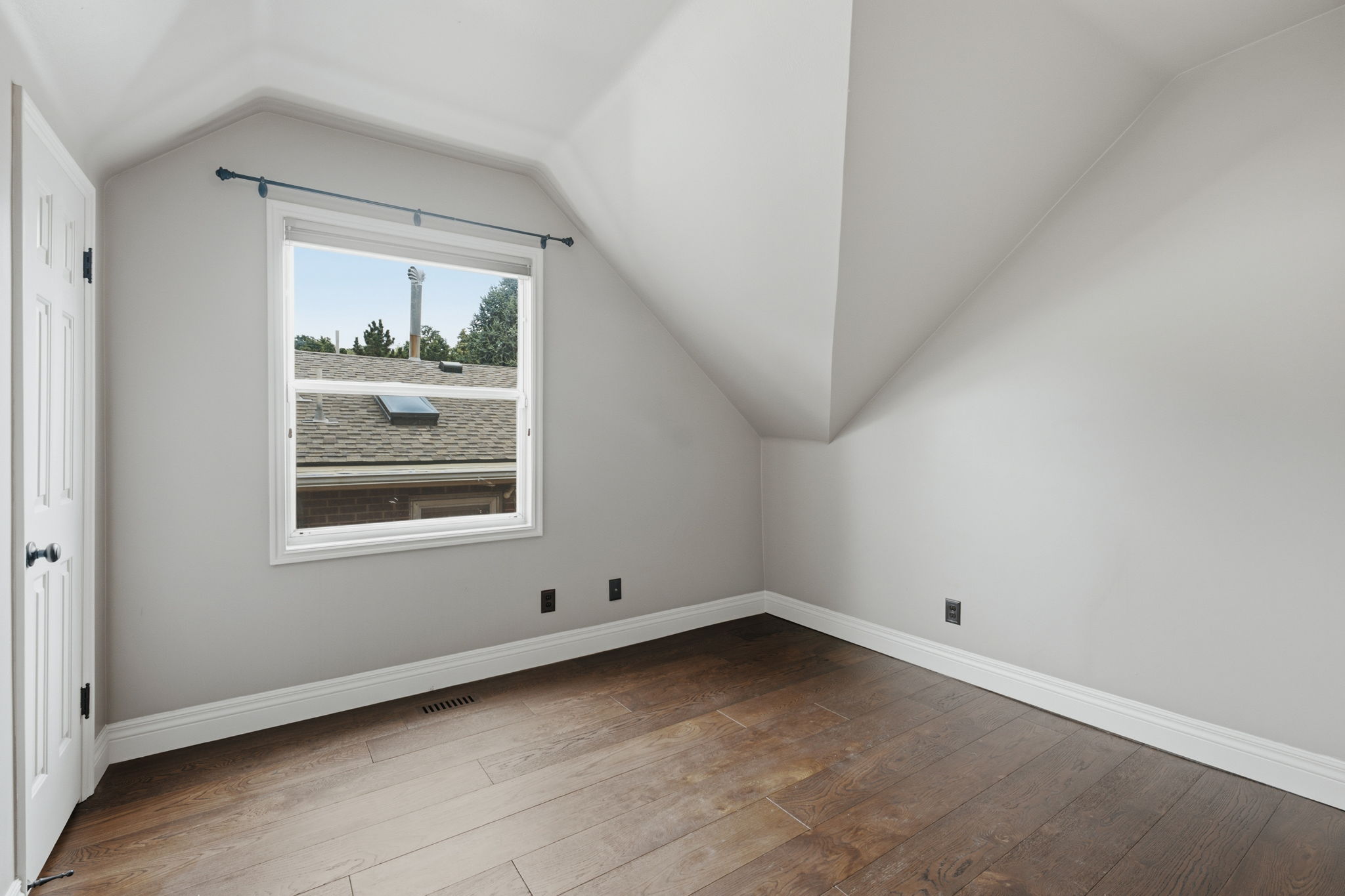 Room featuring wood-finish flooring, white baseboards, and light gray walls with sloped ceilings