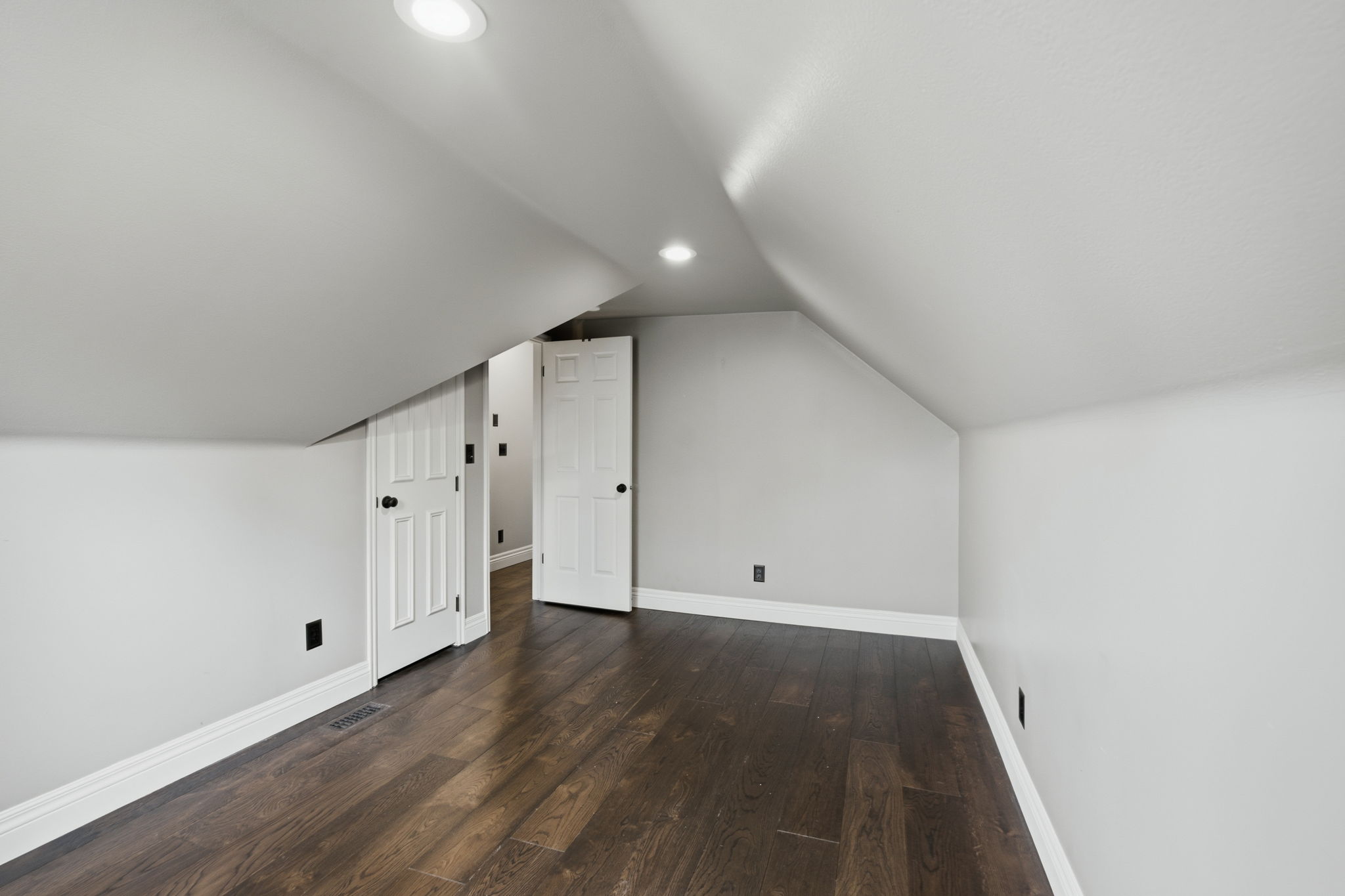 Spacious room featuring dark wood-finish flooring, recessed lighting, crisp white trim, and light gray walls