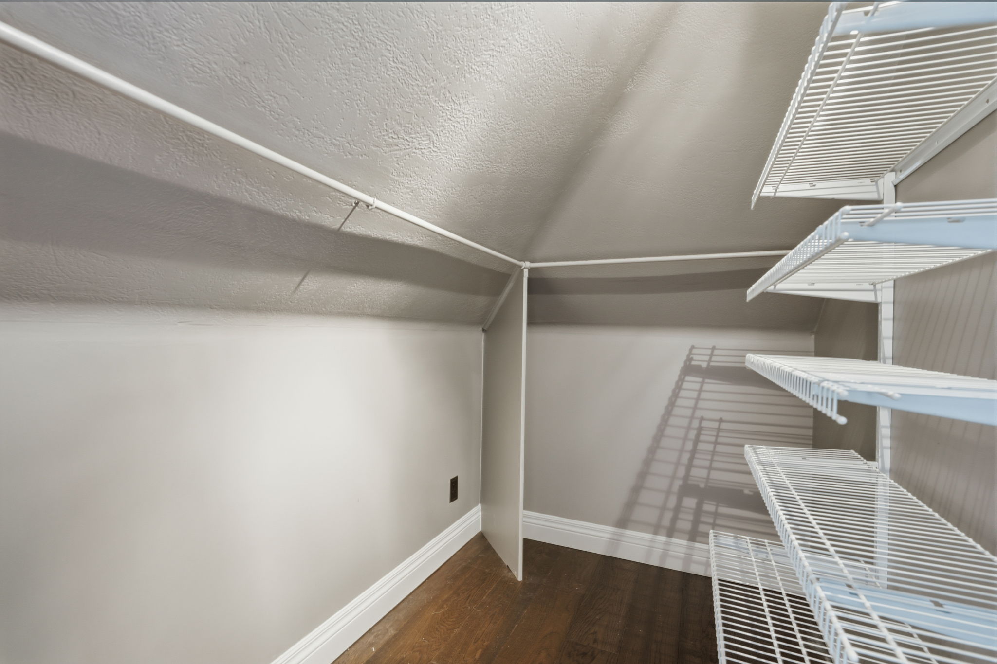 Angled ceiling closet featuring wire shelving, wood-finish flooring, and painted baseboards