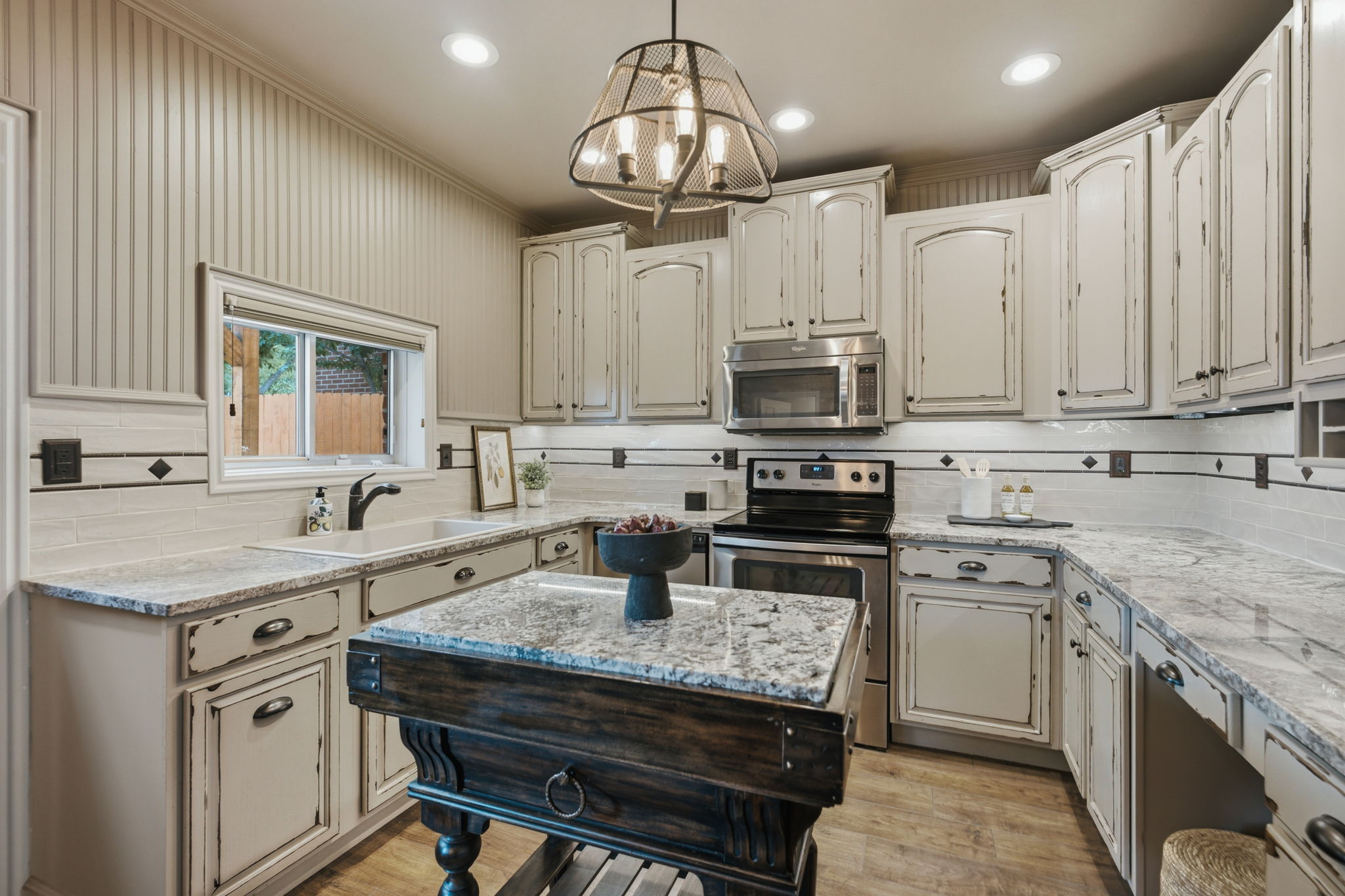 Kitchen featuring distressed cabinetry, stone countertops, a tile backsplash with decorative accents, a central island with a stone surface, and wood-finish flooring