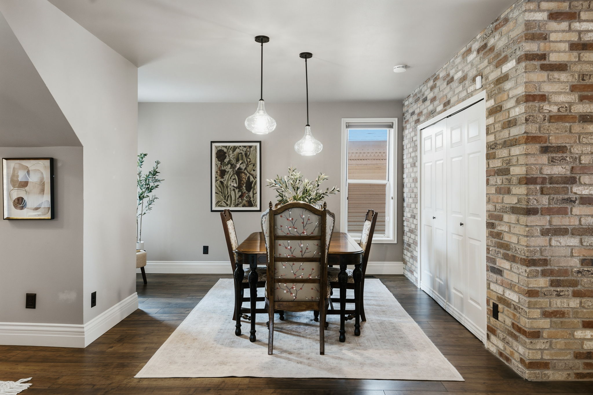 Dining area featuring dark wood-finish flooring, light grey walls, and a prominent brick accent wall