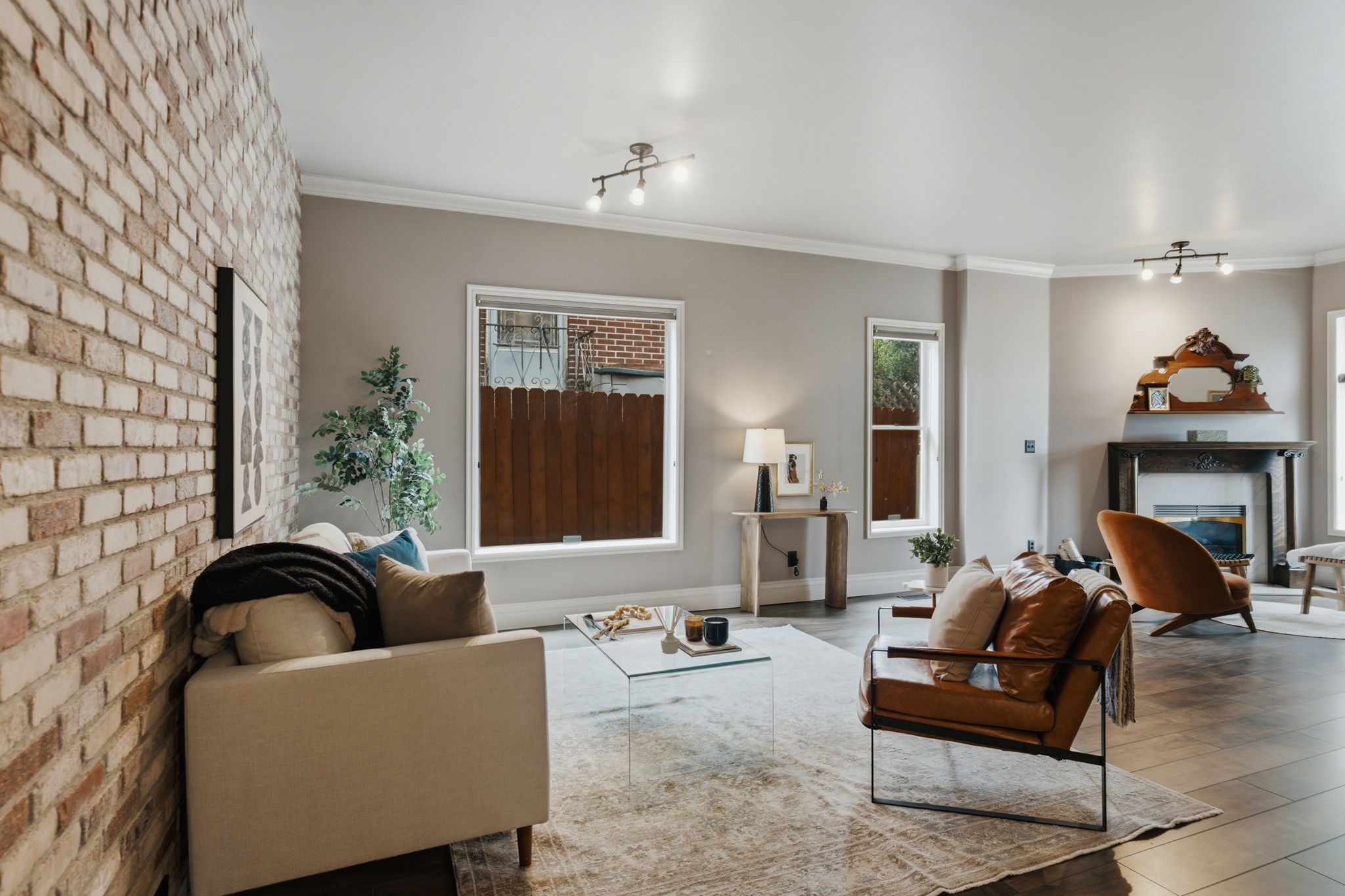 Living area featuring an exposed brick accent wall, wood-finish flooring, multiple windows, crown molding, and a fireplace with a decorative mantel