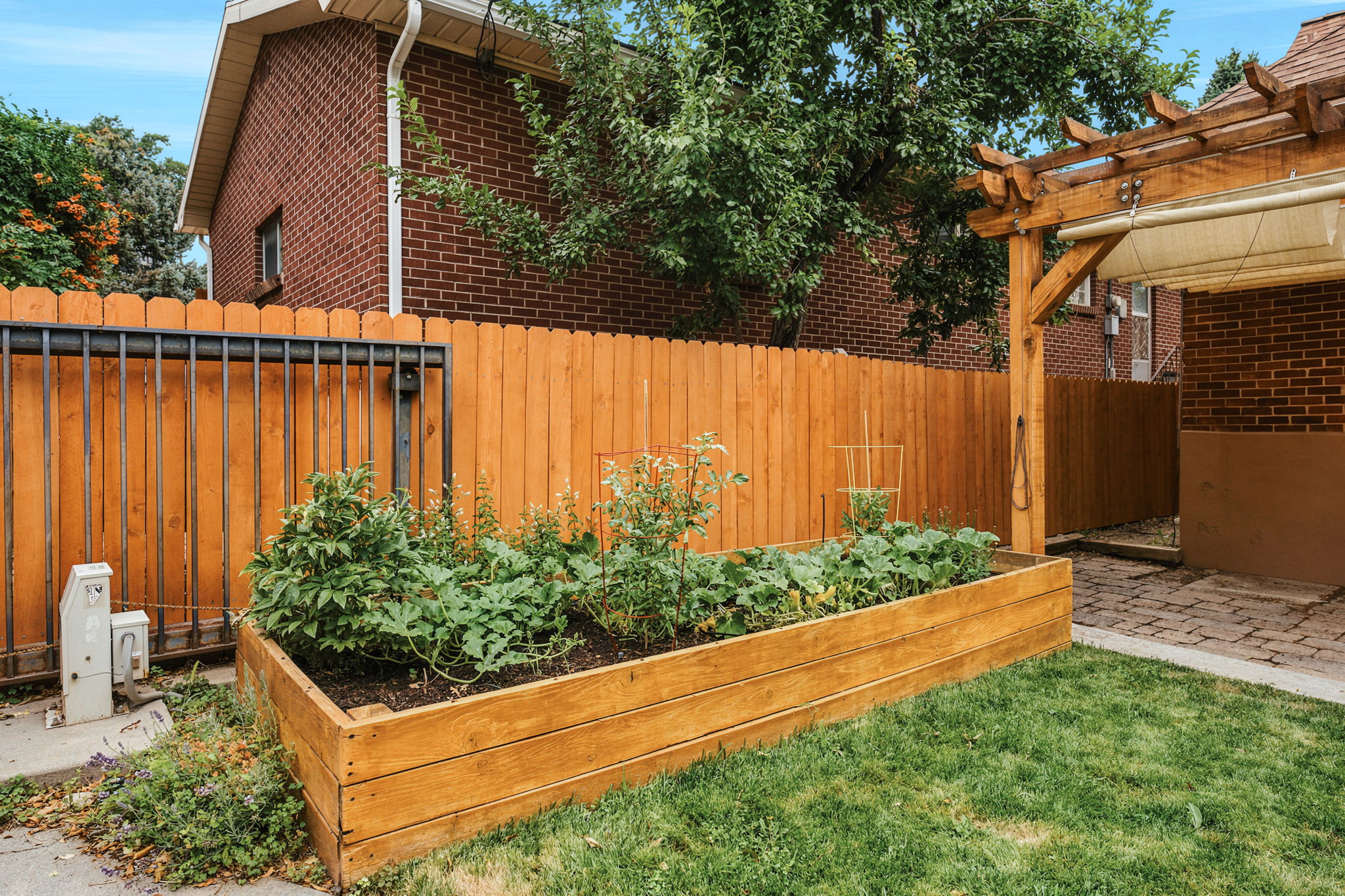 Backyard featuring a raised garden bed, wood privacy fencing, a wood pergola, and a brick-paved patio area