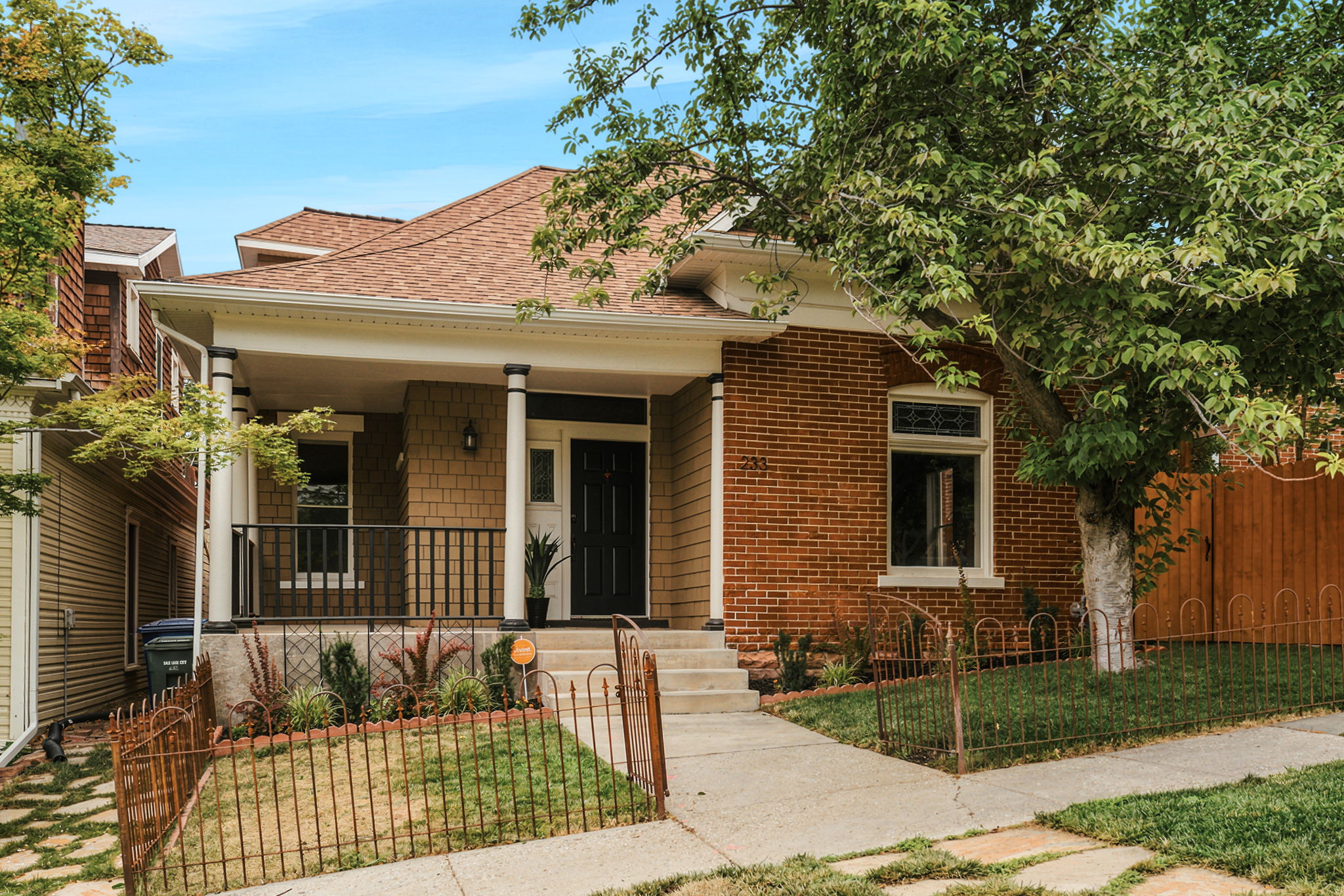 Traditional brick and shingle-sided home featuring a covered front porch with white columns and black railing