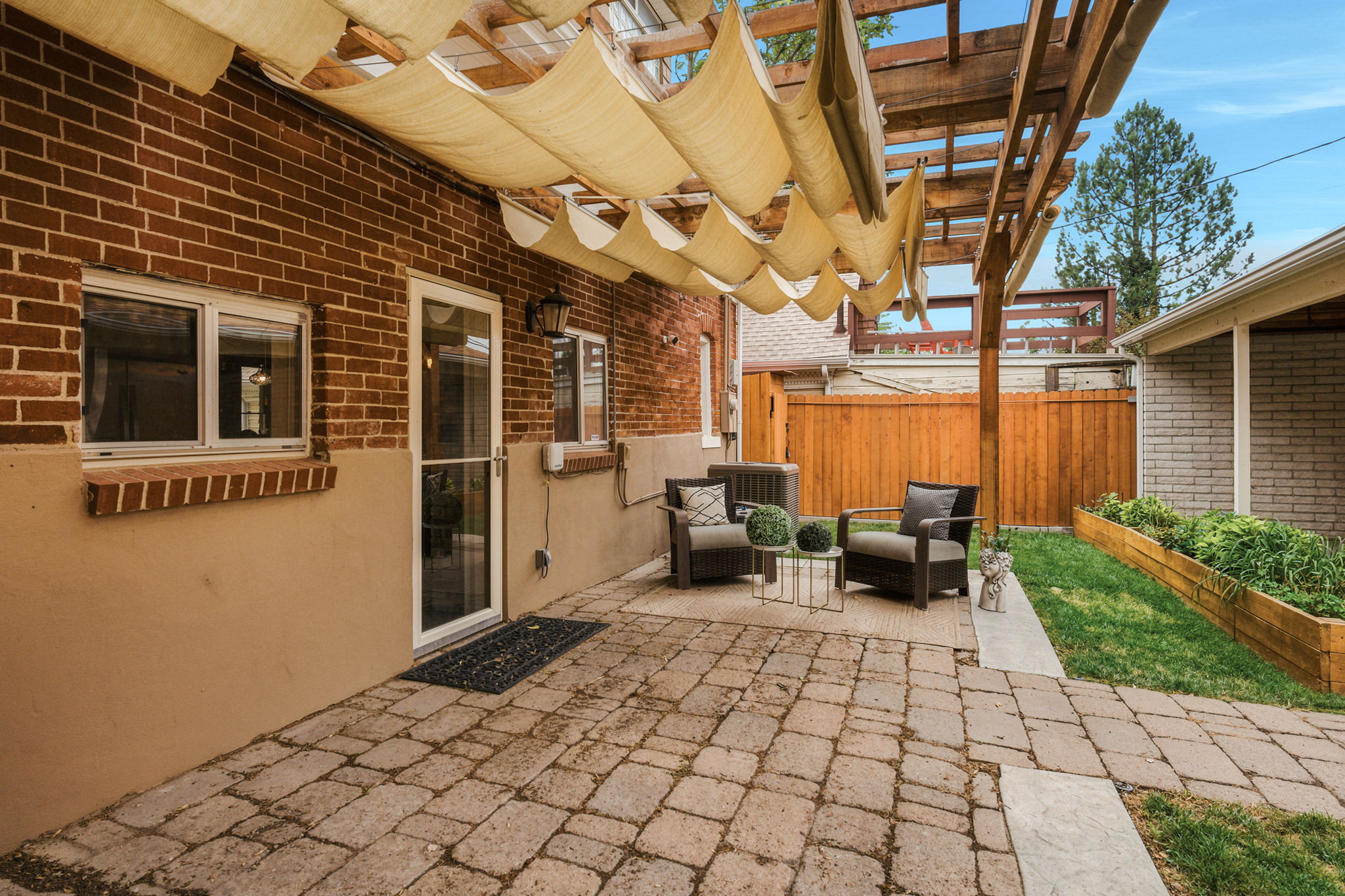 Spacious paver patio featuring a wood pergola with fabric shading, brick exterior walls, and a private wooden fence