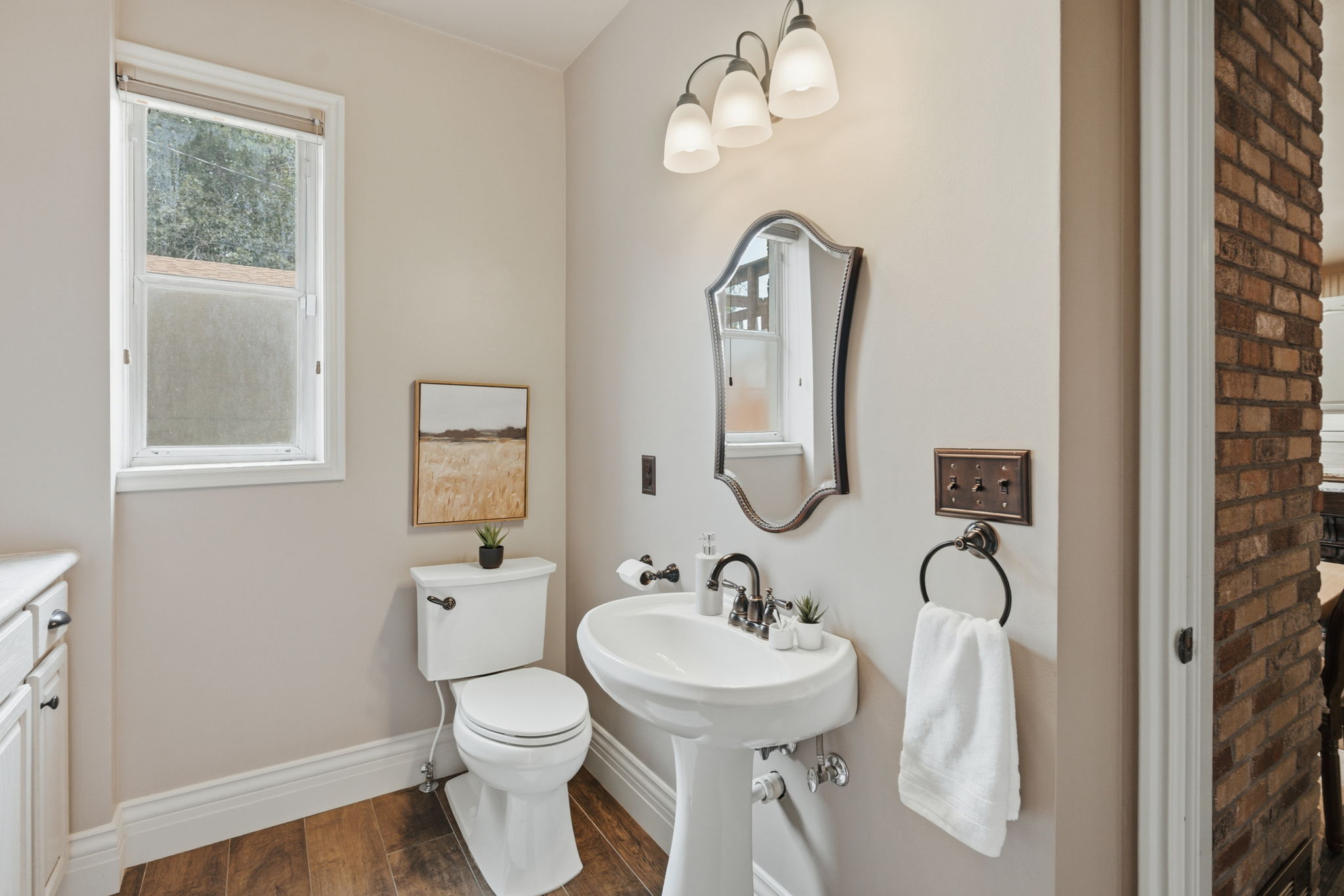Pedestal sink with dark-finish faucet, framed mirror, and three-light vanity fixture