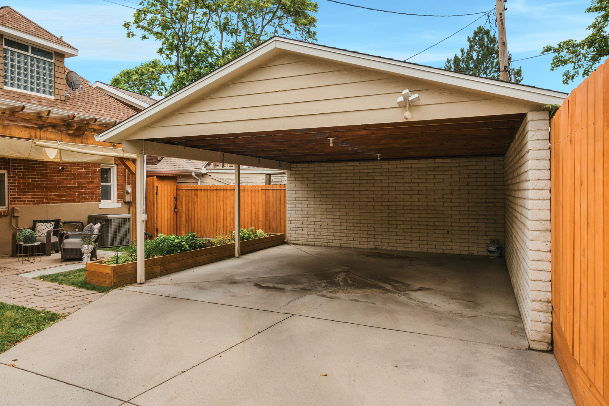 Covered carport with concrete flooring, brick wall, and wood-paneled ceiling