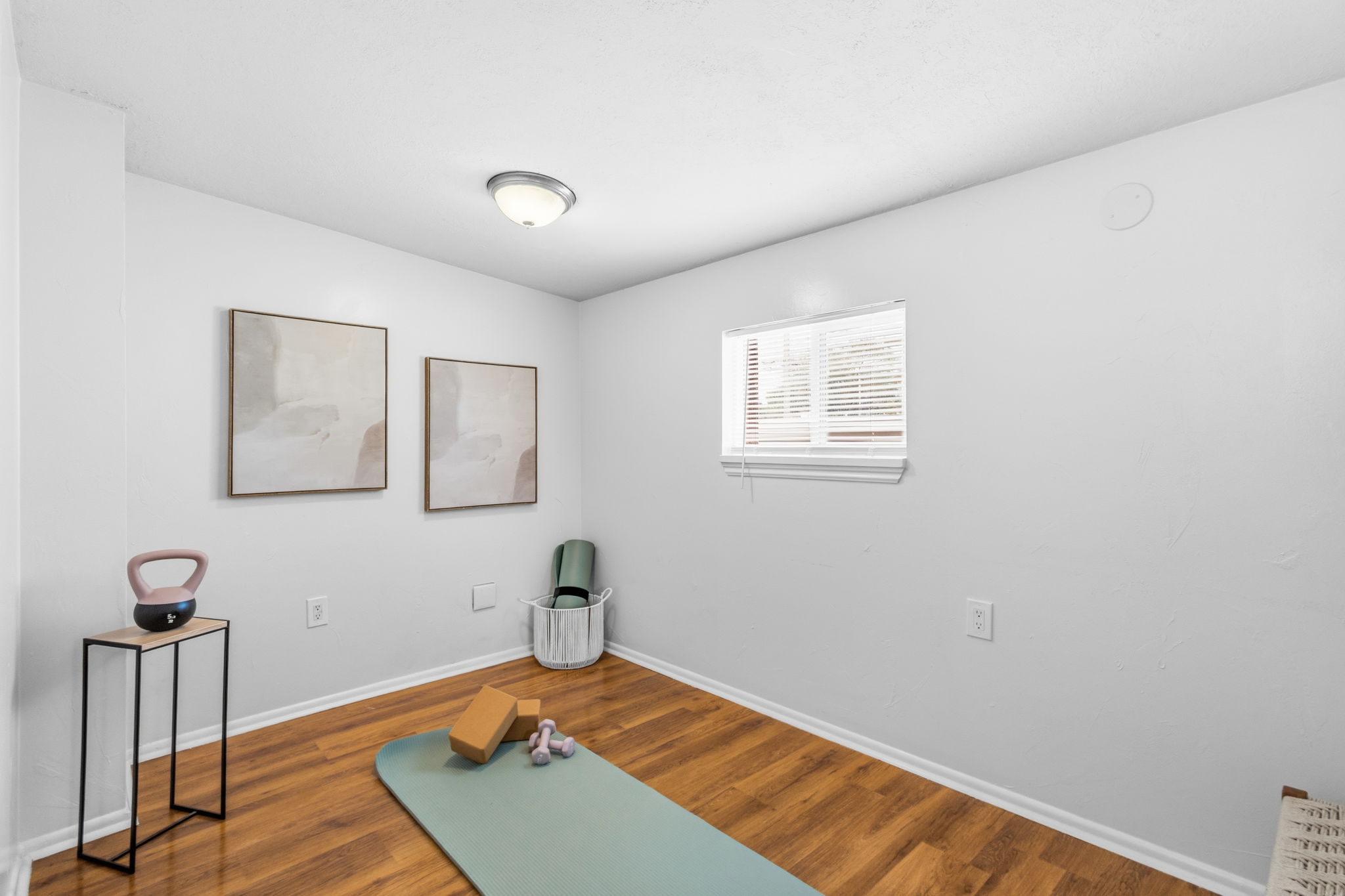 Room with wood-finish flooring, white walls, and a single window with blinds