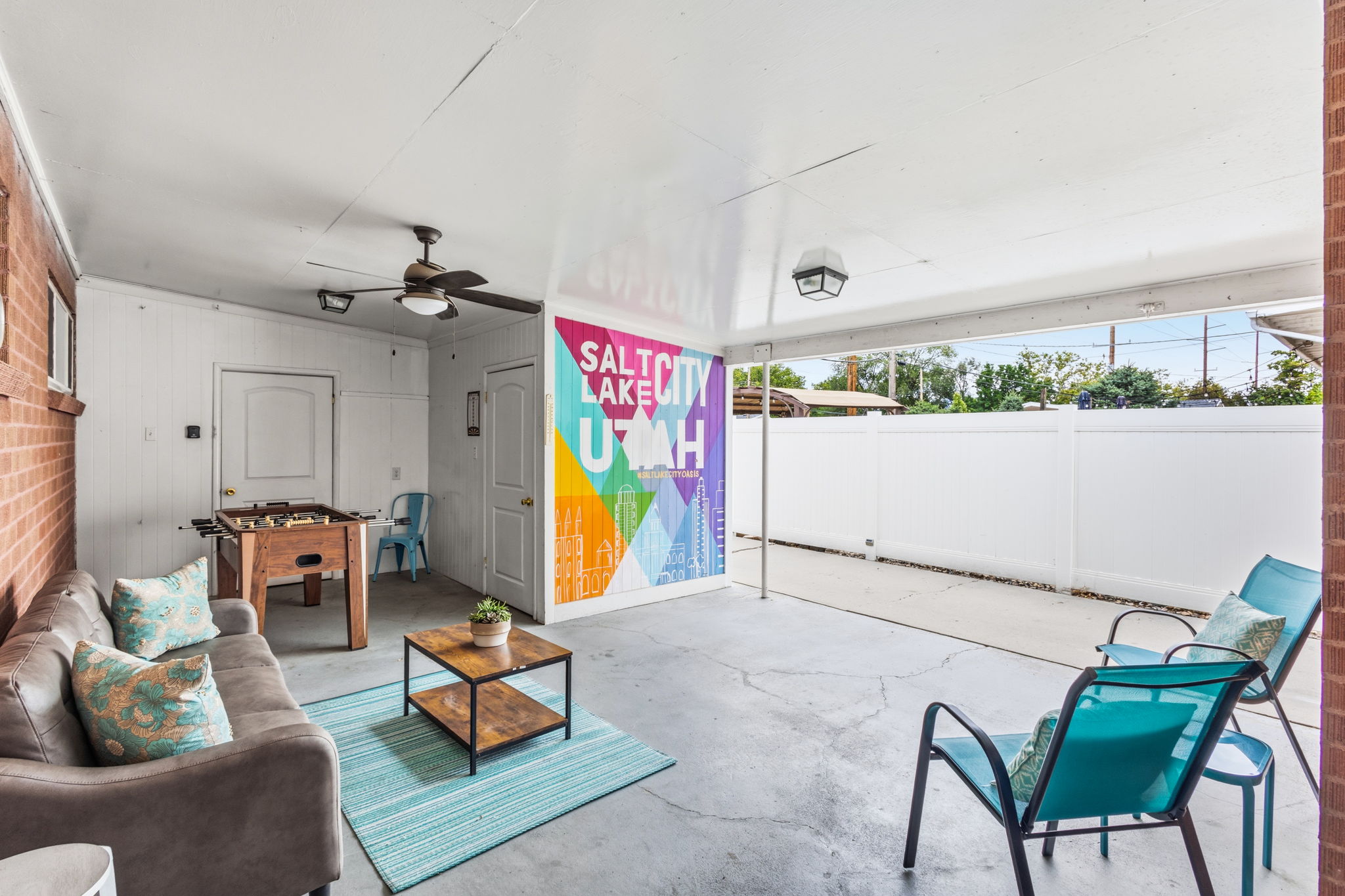 Covered patio featuring a ceiling fan, exposed brick accent wall, concrete flooring, and an exterior privacy fence