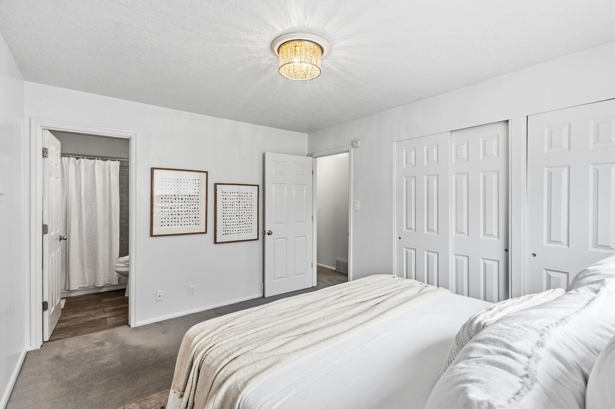 Bedroom with a modern chandelier light fixture, soft gray carpet flooring, and two white panel doors leading to a closet