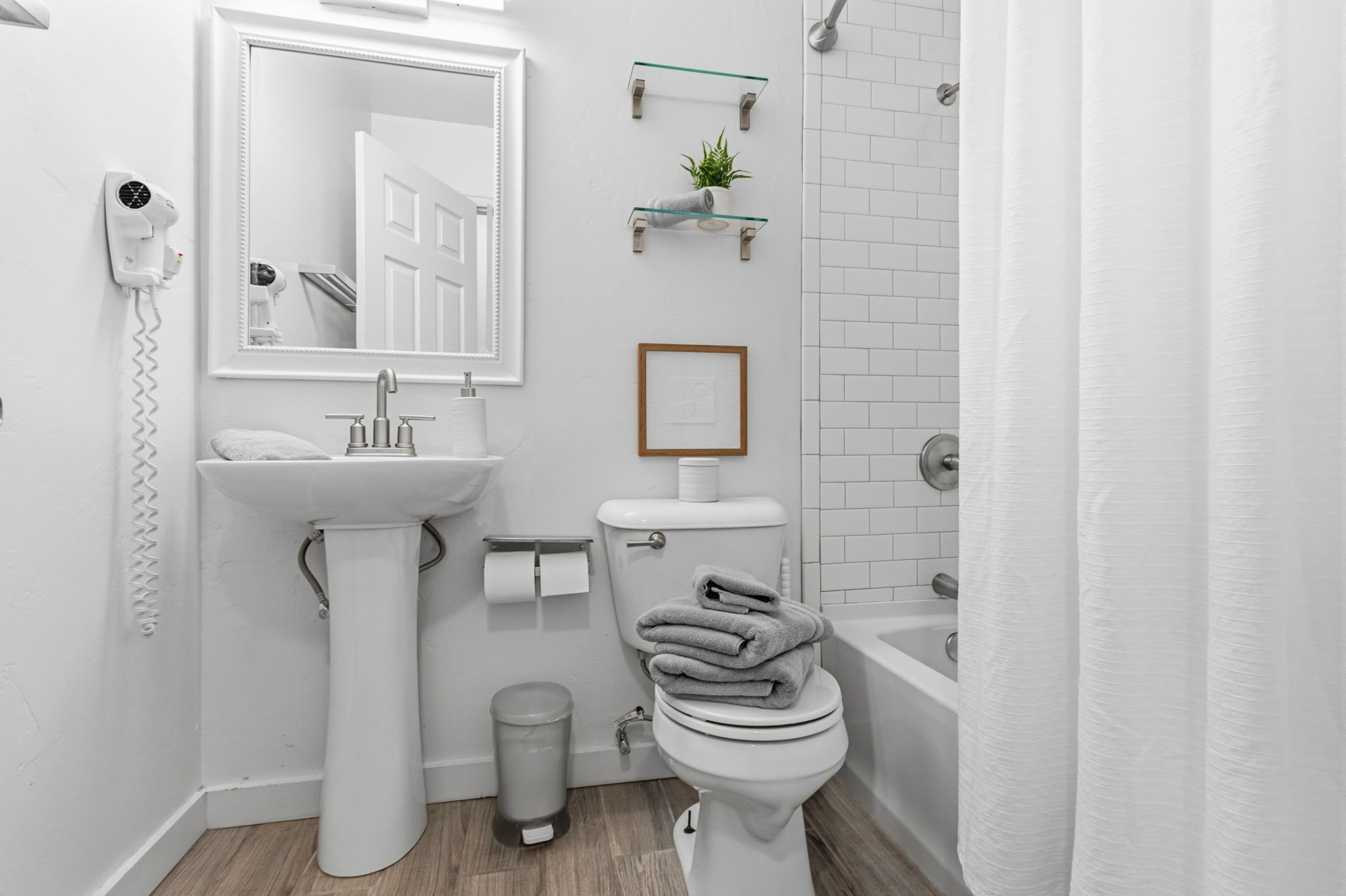 Bathroom featuring a pedestal sink with a framed mirror, a toilet, and a bathtub with subway tile surround
