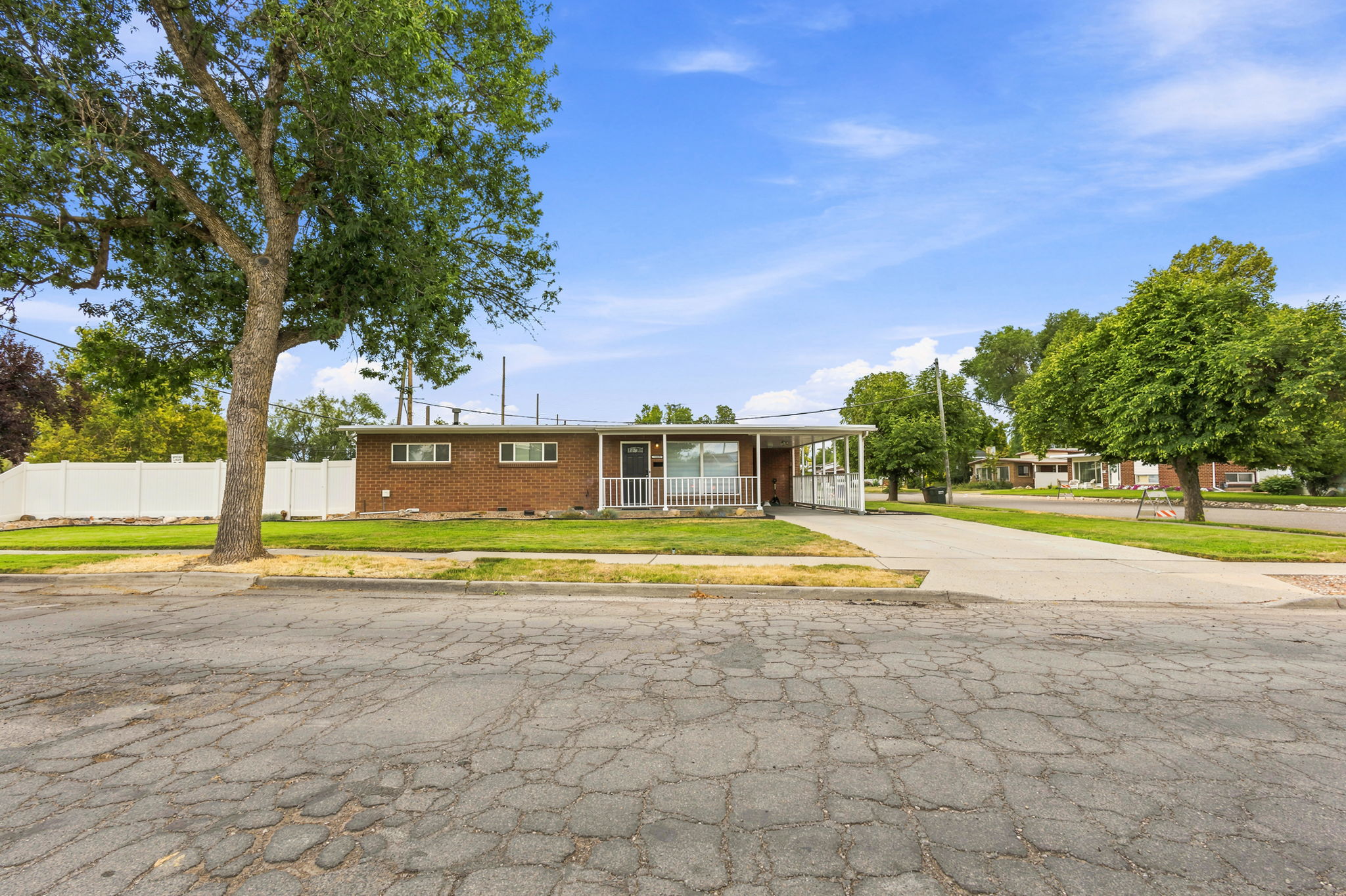 Brick facade home featuring a covered front porch, white railing, and a carport