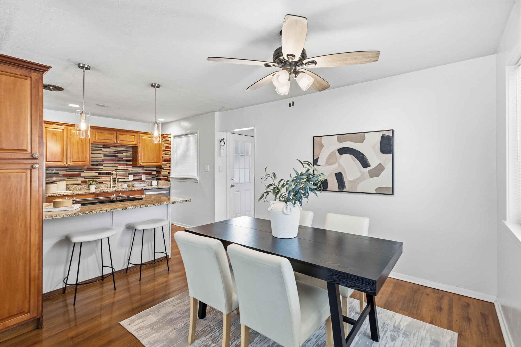 Open-concept living space featuring wood-finish flooring, a kitchen with granite countertops, a mosaic tile backsplash, and a breakfast bar with pendant lighting