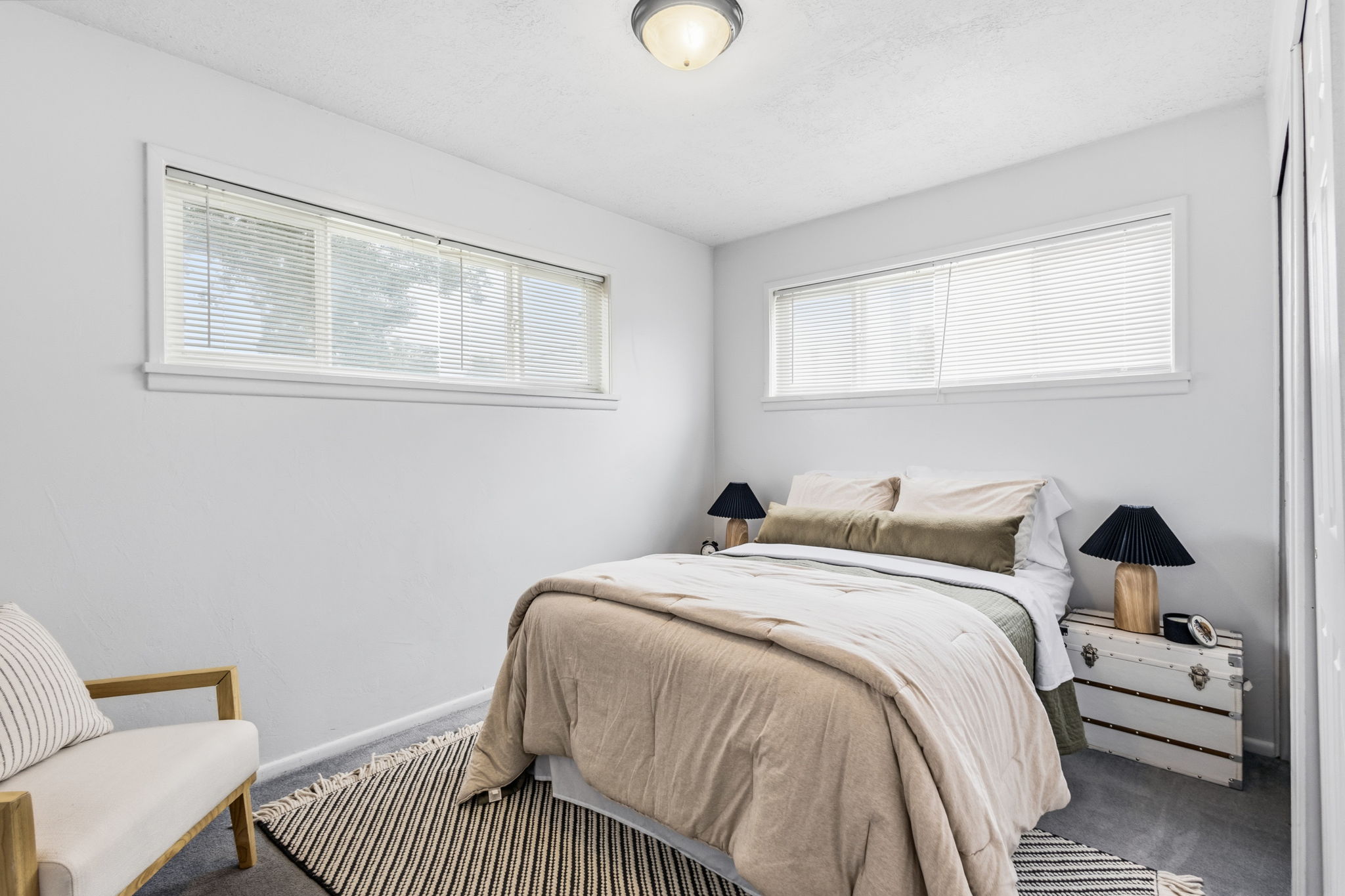 Bedroom featuring two sets of horizontal windows with blinds, light gray wall paint, and gray carpet flooring