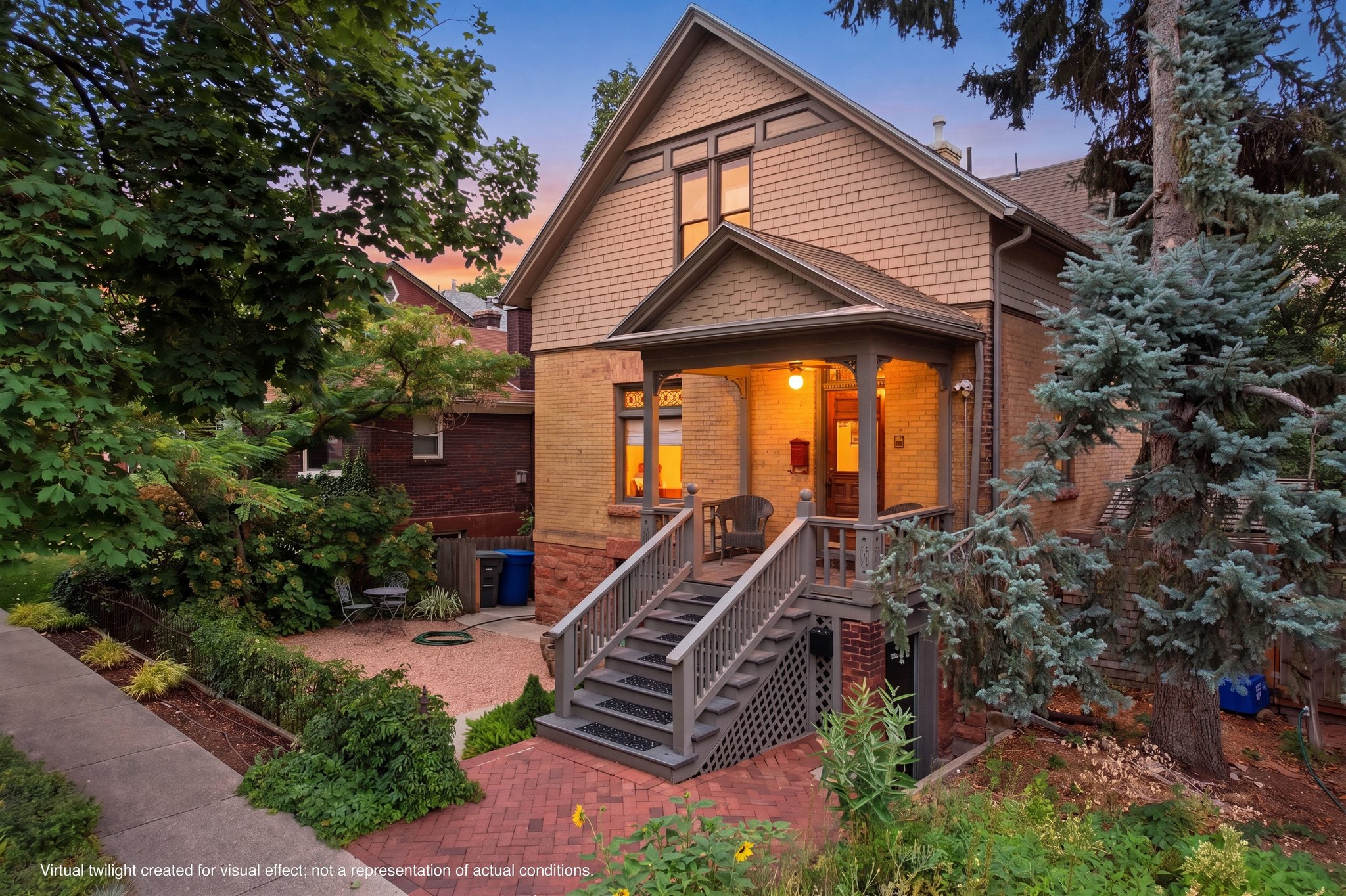 Charming brick and shingle-sided residence featuring a covered front porch, exterior staircase with wooden railings, and mature landscaping