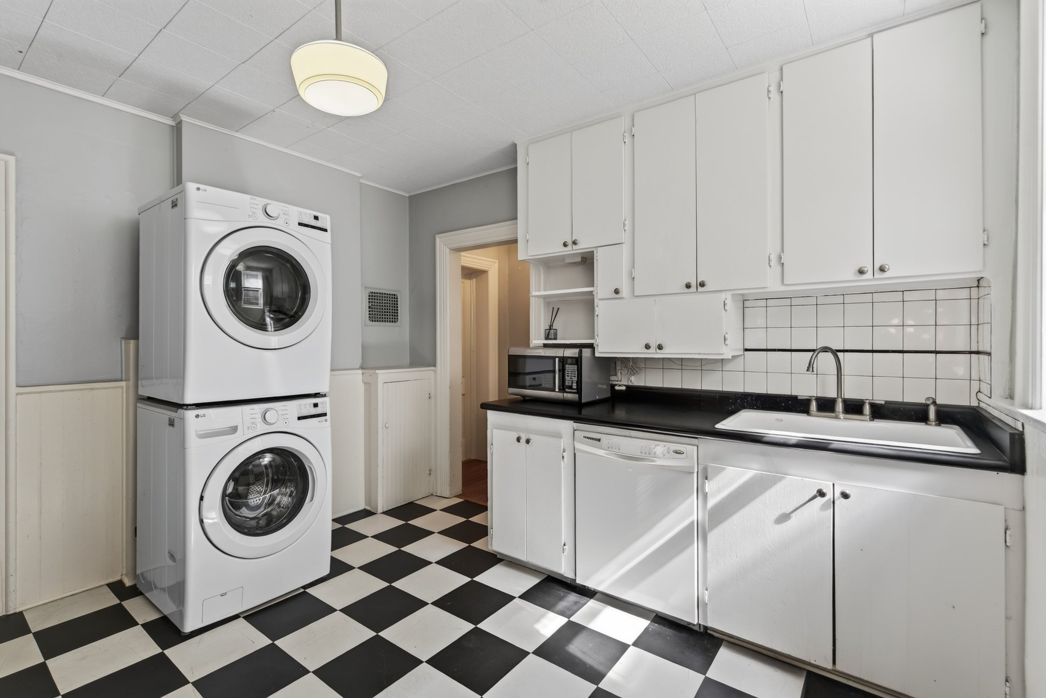 Kitchen area featuring stacked white washer and dryer, checkerboard flooring, white cabinetry, dark countertops, and a white tiled backsplash