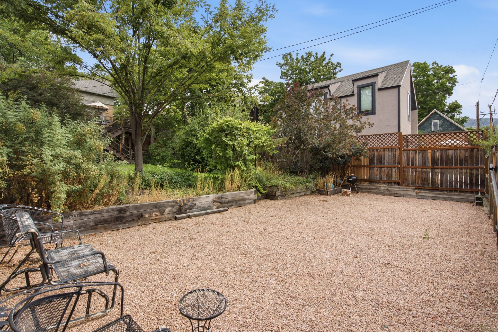 Spacious gravel yard featuring a wood privacy fence, lattice top extension, and natural landscaping along the perimeter