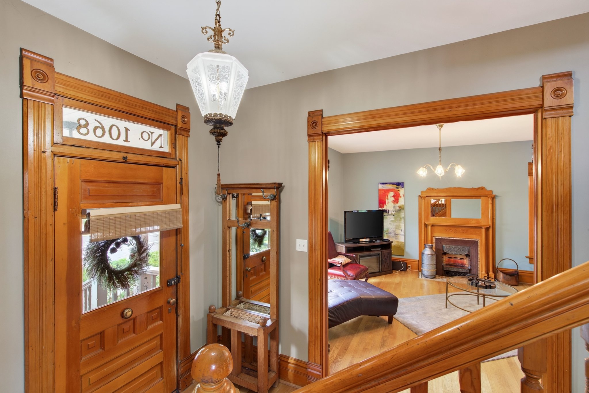 Rich wood-paneled entry door with transom window, ornate overhead light fixture, and wood-finish flooring